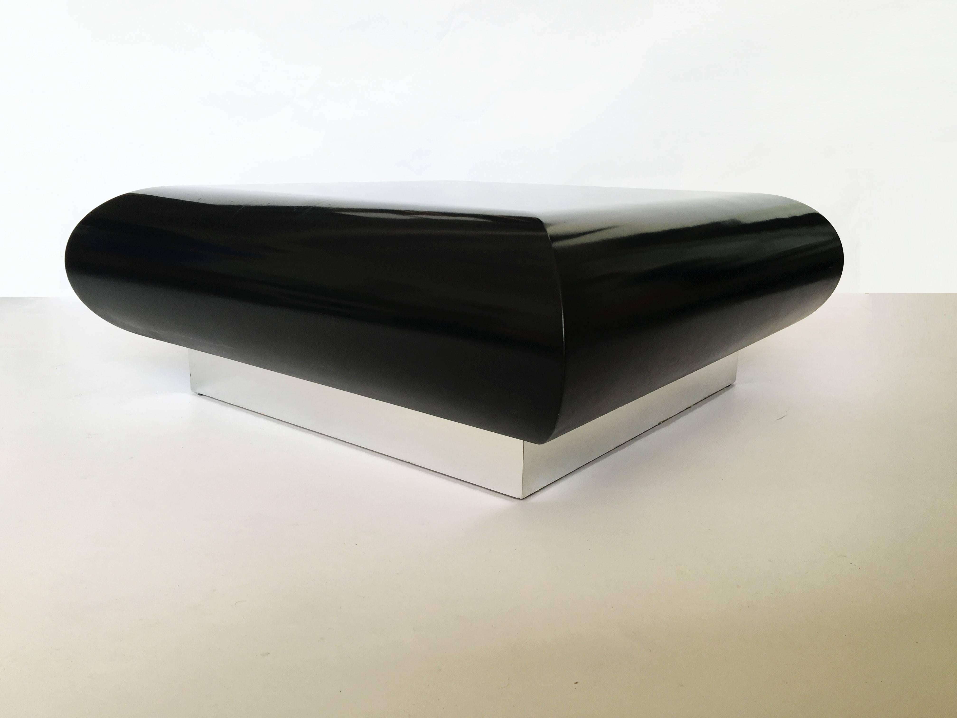 This glamorous coffee table features large black lacquer square shape with deeply curved edges resting on a chrome plinth base.
 