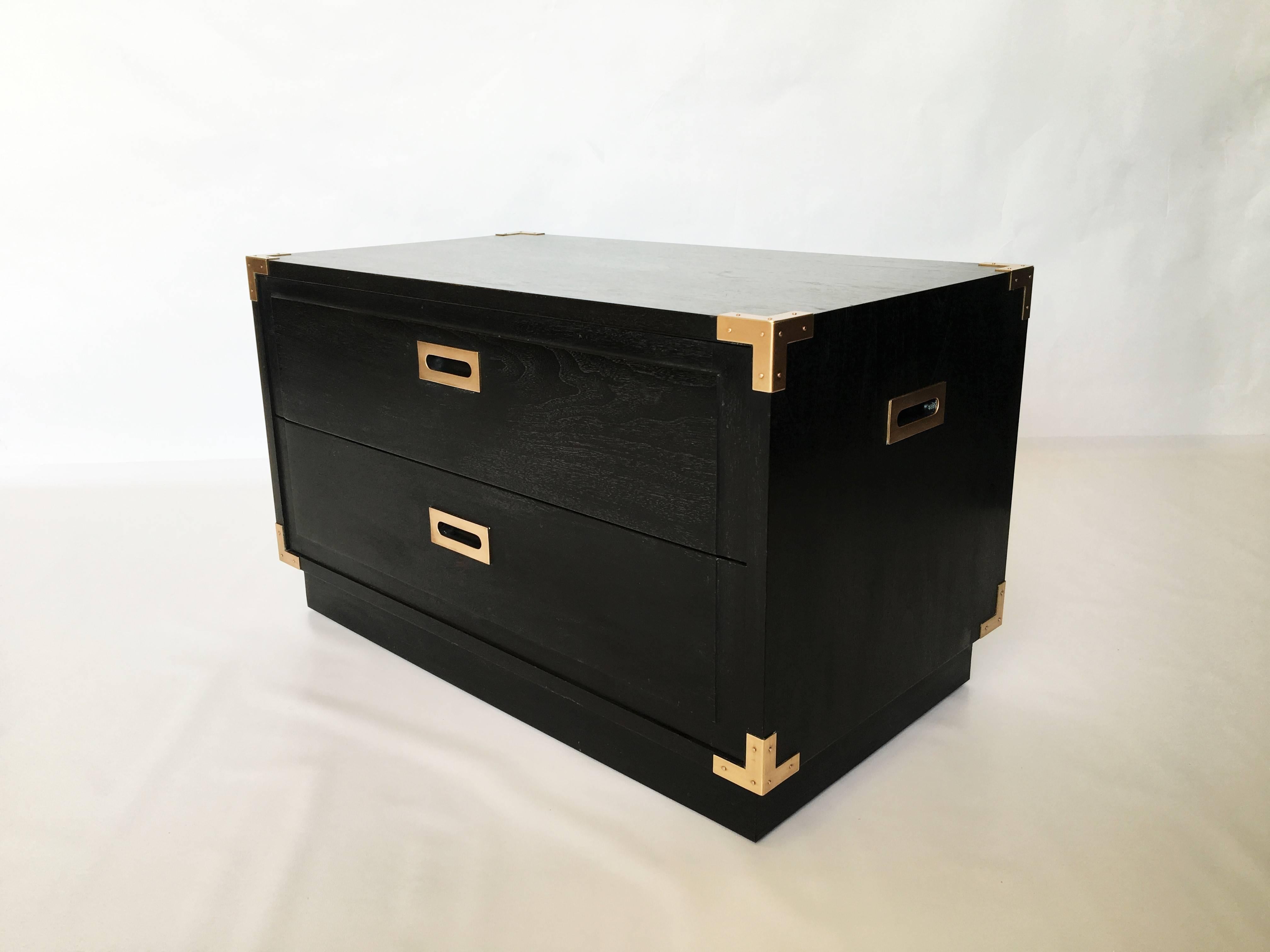 Gorgeous pair of midcentury Campaign style ebonized nightstands/ end tables. Accenting the are copper tone brass corner pieces and hardware. Includes two equal sized drawers, each with recessed pull handles, two recessed handles on either side are