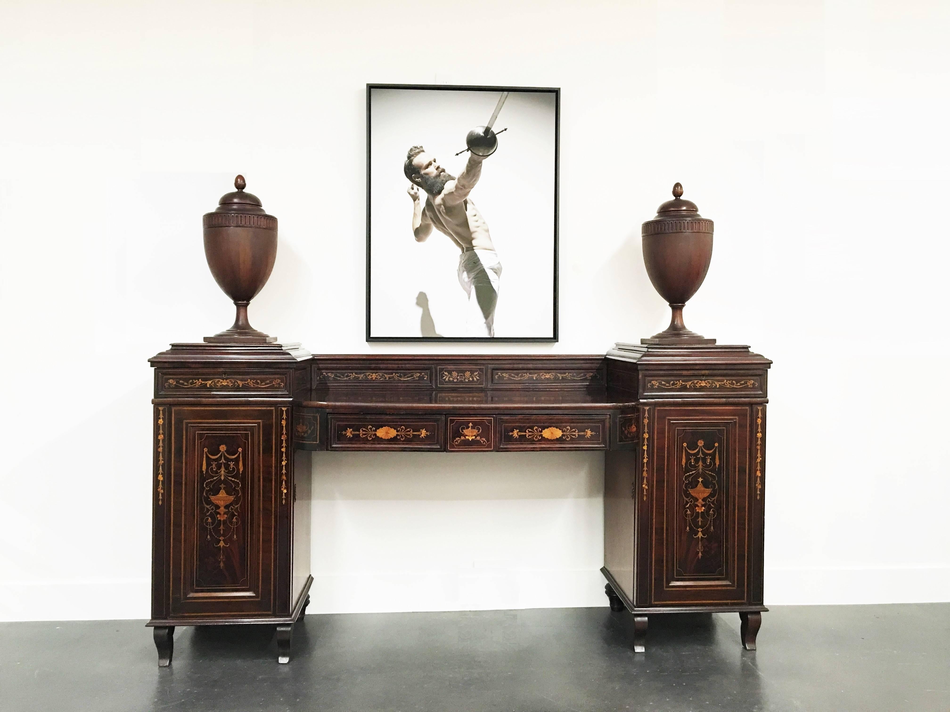 Decorated throughout with fine quality marquetry of pale woods inset into a contrasting rosewood ground showing floral arrangements, vases and garlands. The sideboard comprises a pedestal cupboard at each end topped by a resplendent cutlery urn, the