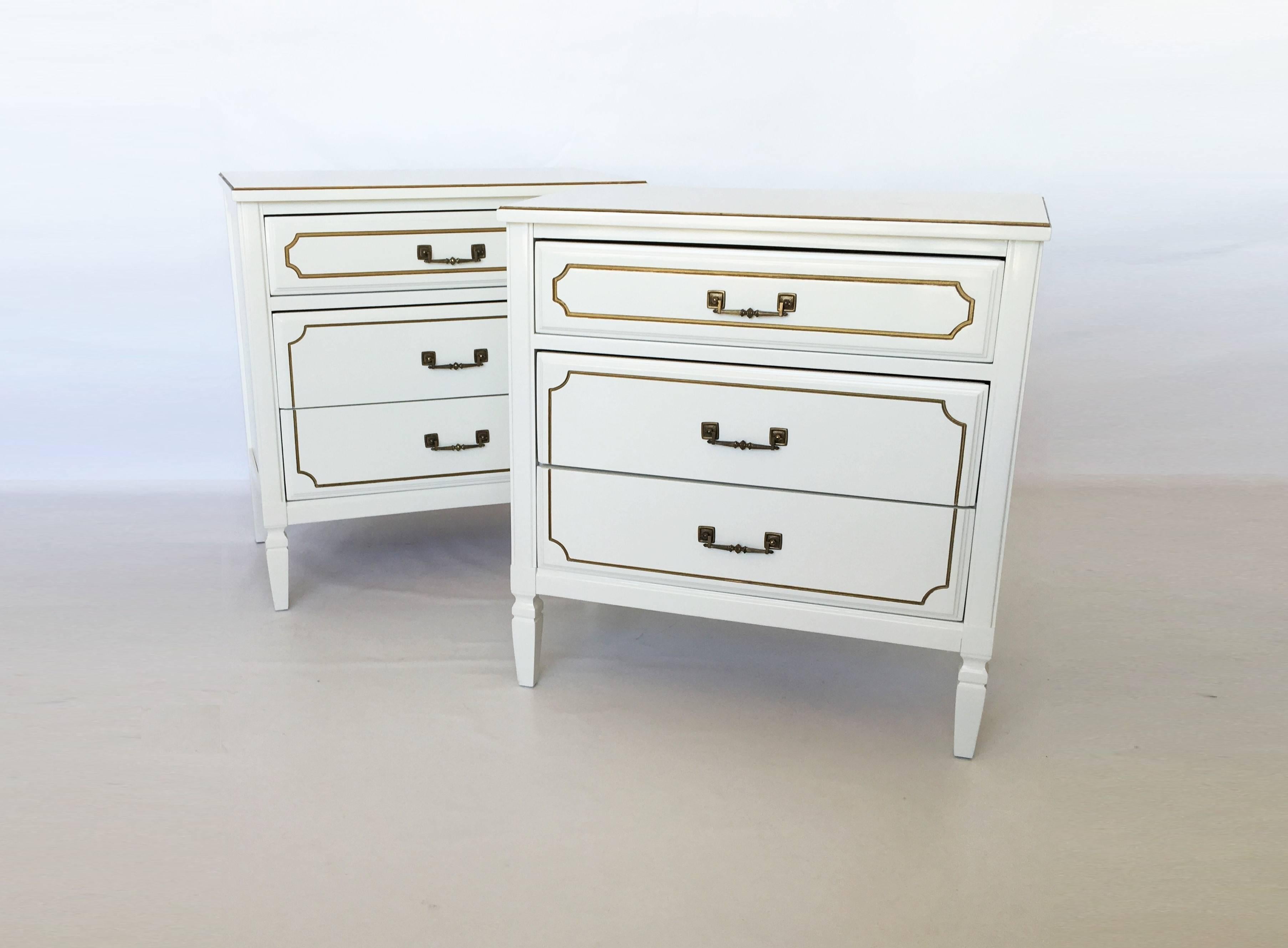 A pair of vintage mid-century French Regency paint decorated chests. Lacquered in soft white. Each night stand features a rectangular top overhanging three stacked inset drawers with dovetail joinery. The commodes rise on tapering feet. The drawer