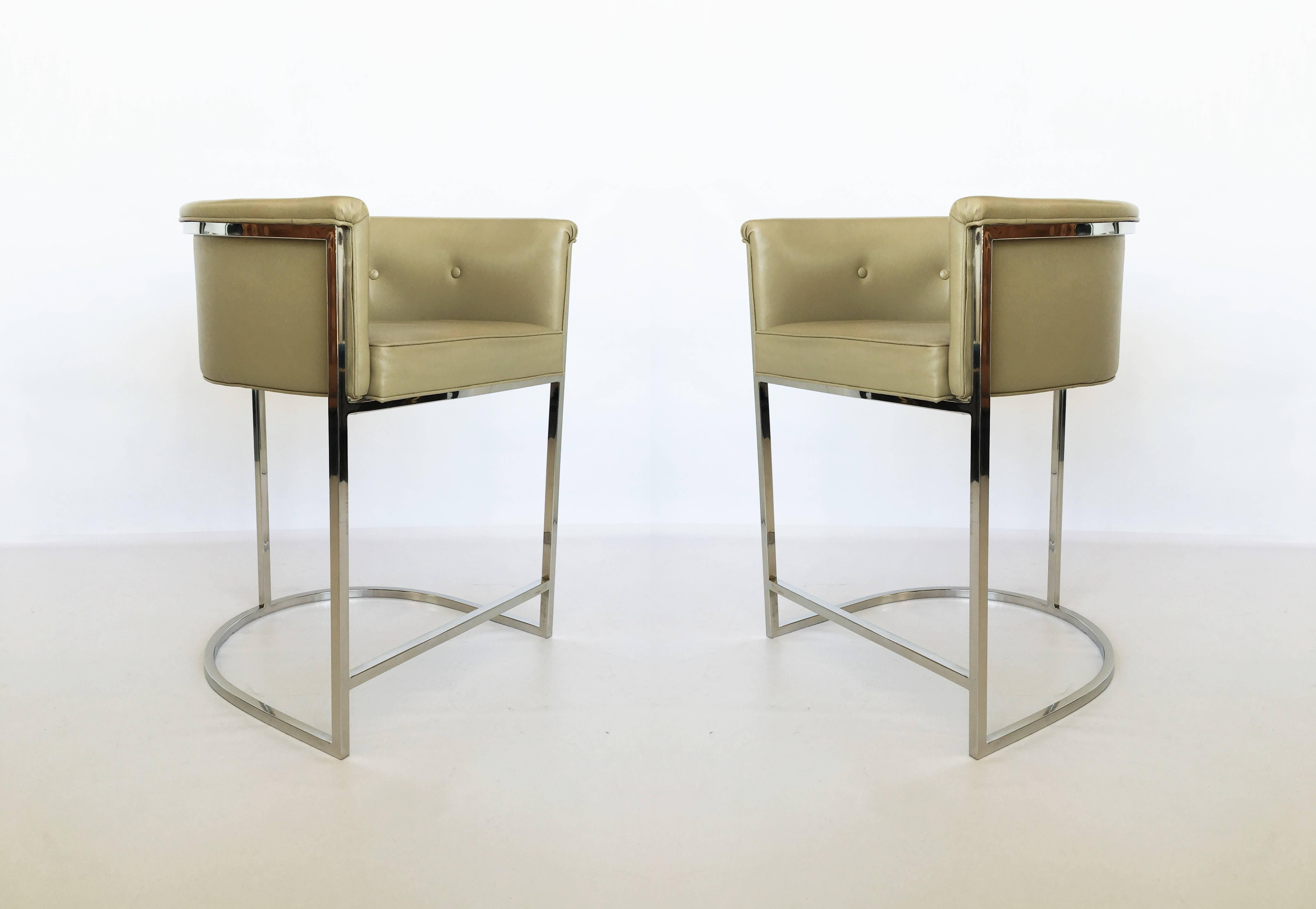 These classic barrel back design bar stools were designed in the 1970s in the style of Milo Baughman. Upholstered in a soft neutral colored leather on chrome frames with connecting footrest for maximum comfort. They are a versatile size and can be