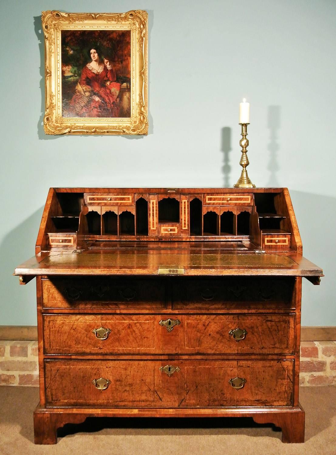 A fine quality George II bureau/slant fronted desk of superior colour and deep original patina and retaining original brass handles.  The three principal graduated drawers dressed with well figured walnut and each inlaid with two featherbanded