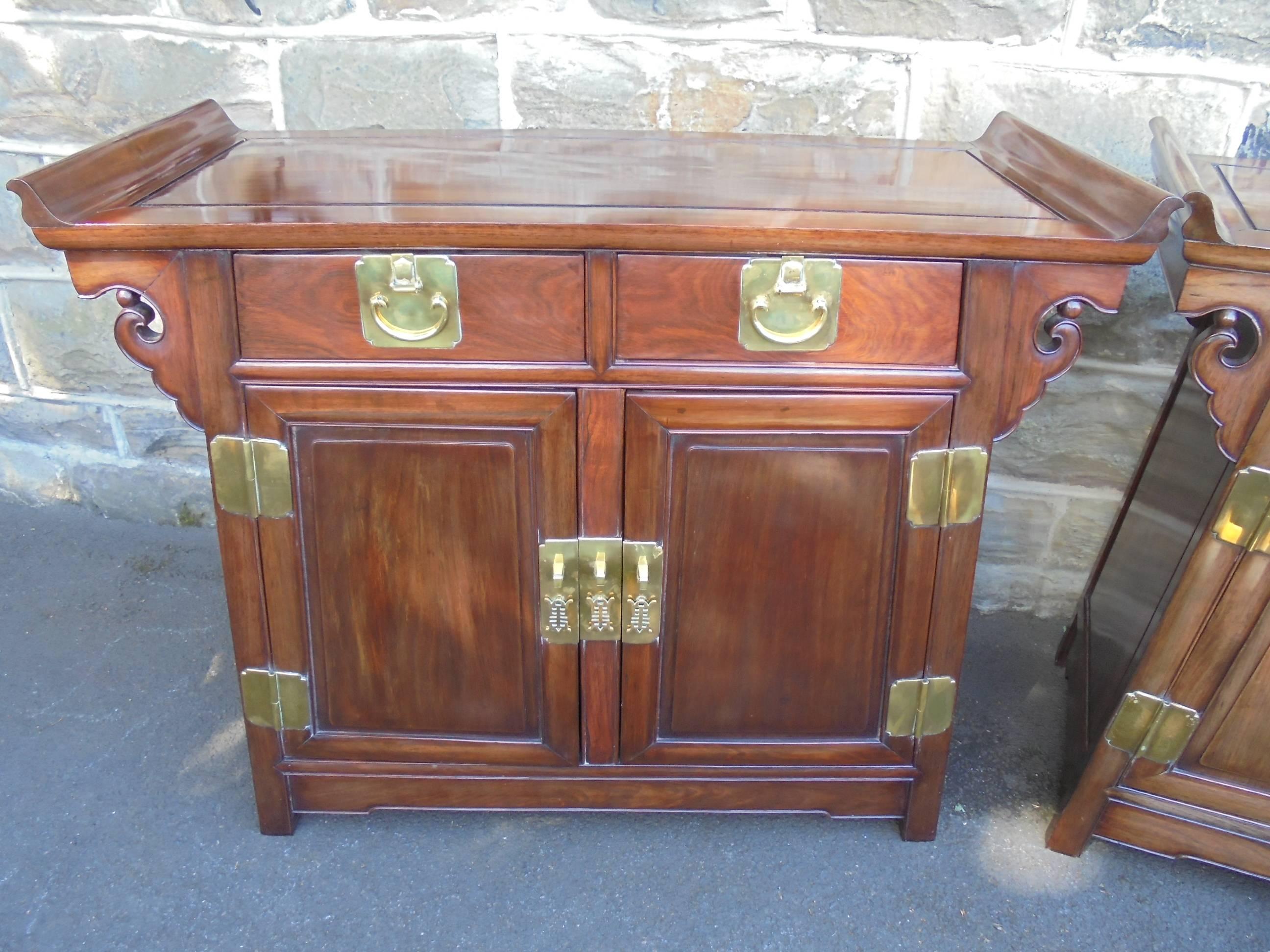 Offered for sale is this good pair of early 20th century Chinese side cabinet. 

Made from a Chinese hardwood possibly rosewood. Oblong top with cleated joint construction, raised curved ends, two draws over two cupboard doors. Good quality brass