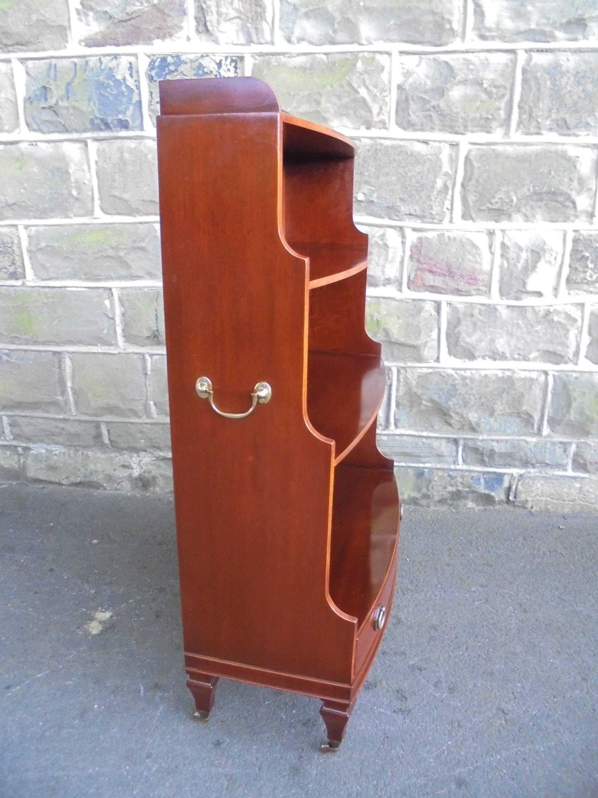 Offered for sale is this mahogany waterfall bookcase.

Made from solid mahogany. Small raised gallery back having fixed shelves with shaped waterfall sides. Brass swan neck carrying handles to each side. Draw to the bottom with brass ring handles,