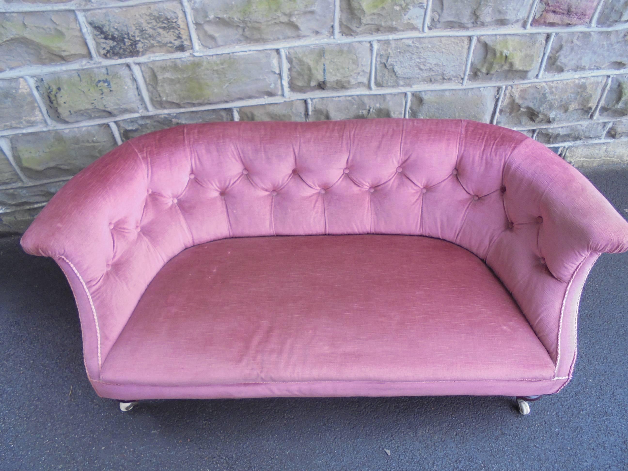 Offered for sale is this lovely shaped small English upholstered sofa/chaise.

Great shape and of good size and dimensions. Shaped arms having button back, covered in a pink fabric standing on turned mahogany legs with original brass and ceramic