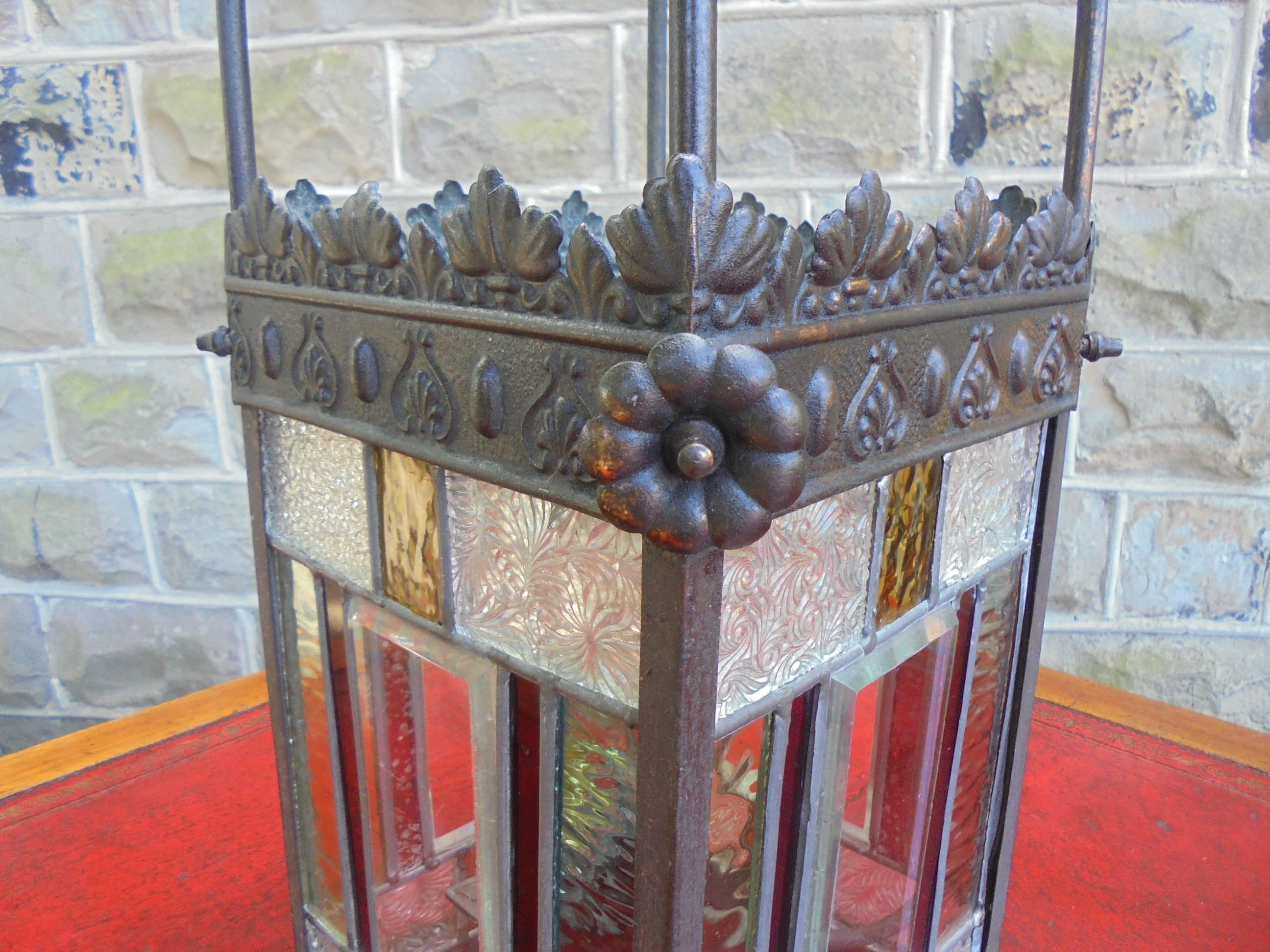 Offered for sale is this antique brass and colored glass hanging lantern.

Victorian, having embossed brass frame which has nice verdigris patination. Plain and color glass leaded panels Originally would have been a gas lamp, still retains its