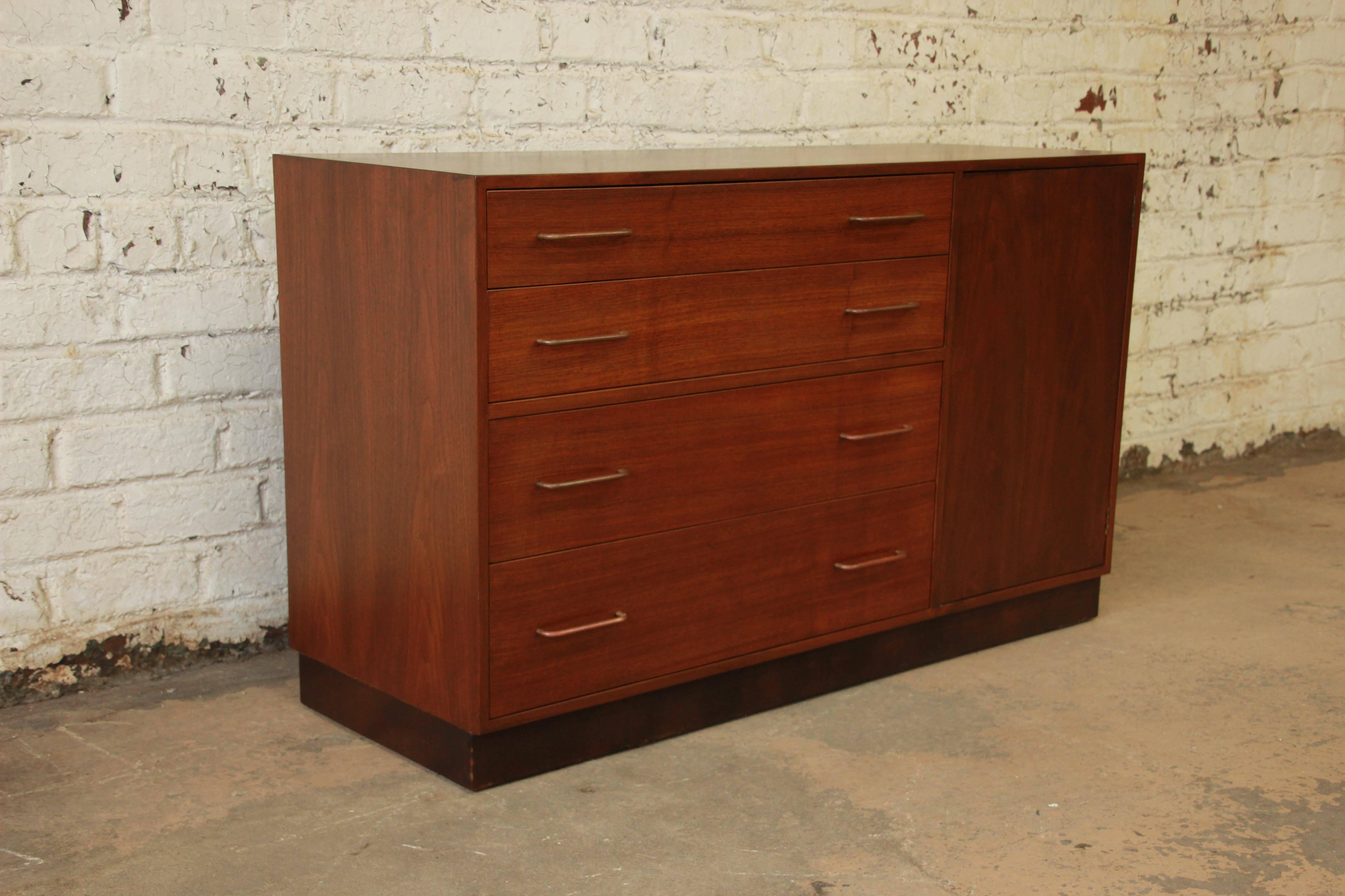 Sleek and stylish Mid-Century Modern sideboard buffet or credenza by Edward Wormley for Dunbar Furniture. The sideboard features clean Minimalist lines and gorgeous walnut wood grain. The walnut case rests on a leather plinth base. The sideboard