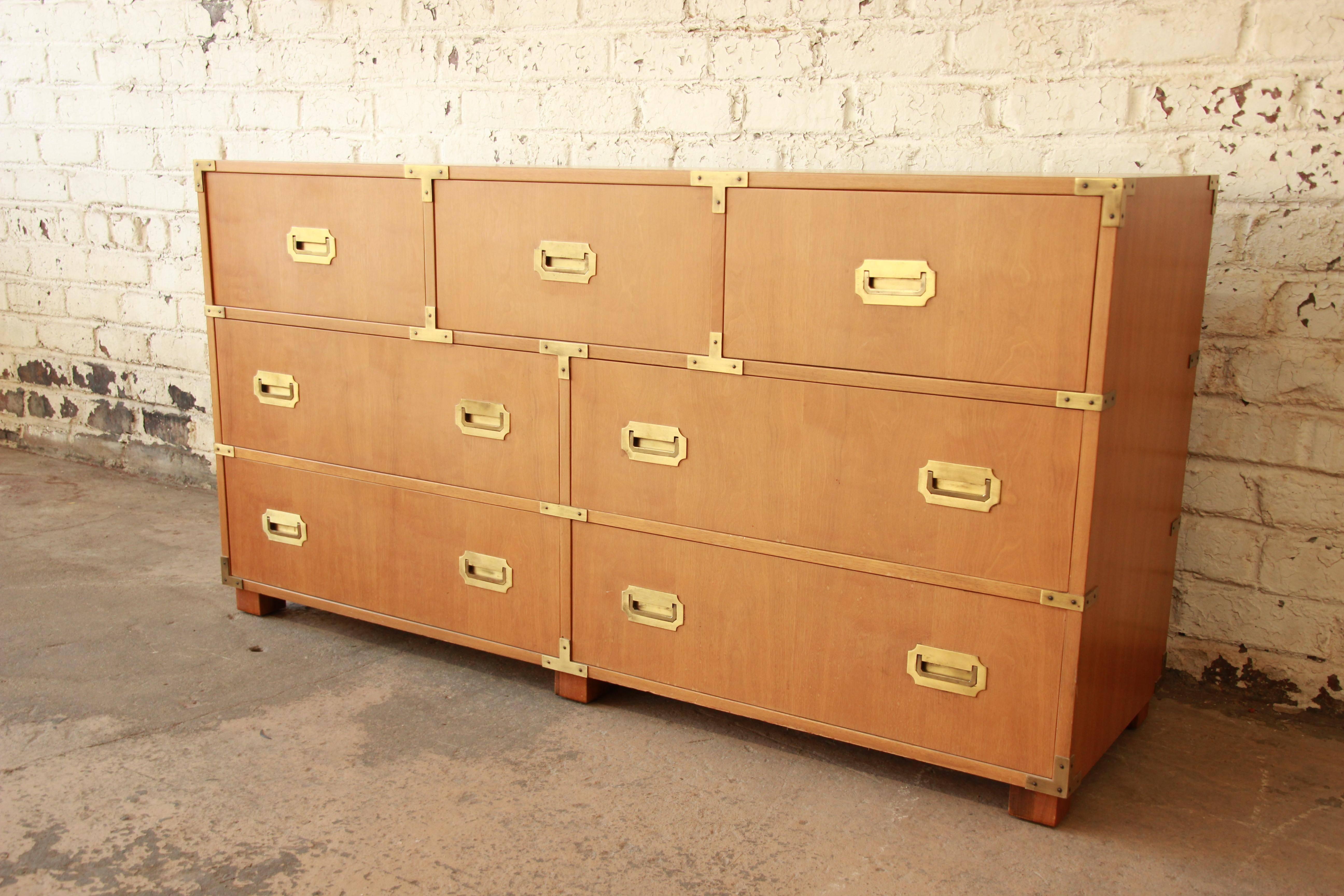 Offering a gorgeous Mid-Century Campaign style chest of drawers by Baker Furniture. The dresser features stunning bleached walnut wood grain and clean brass hardware. It offers ample room for storage with seven deep dovetailed drawers, with a unique