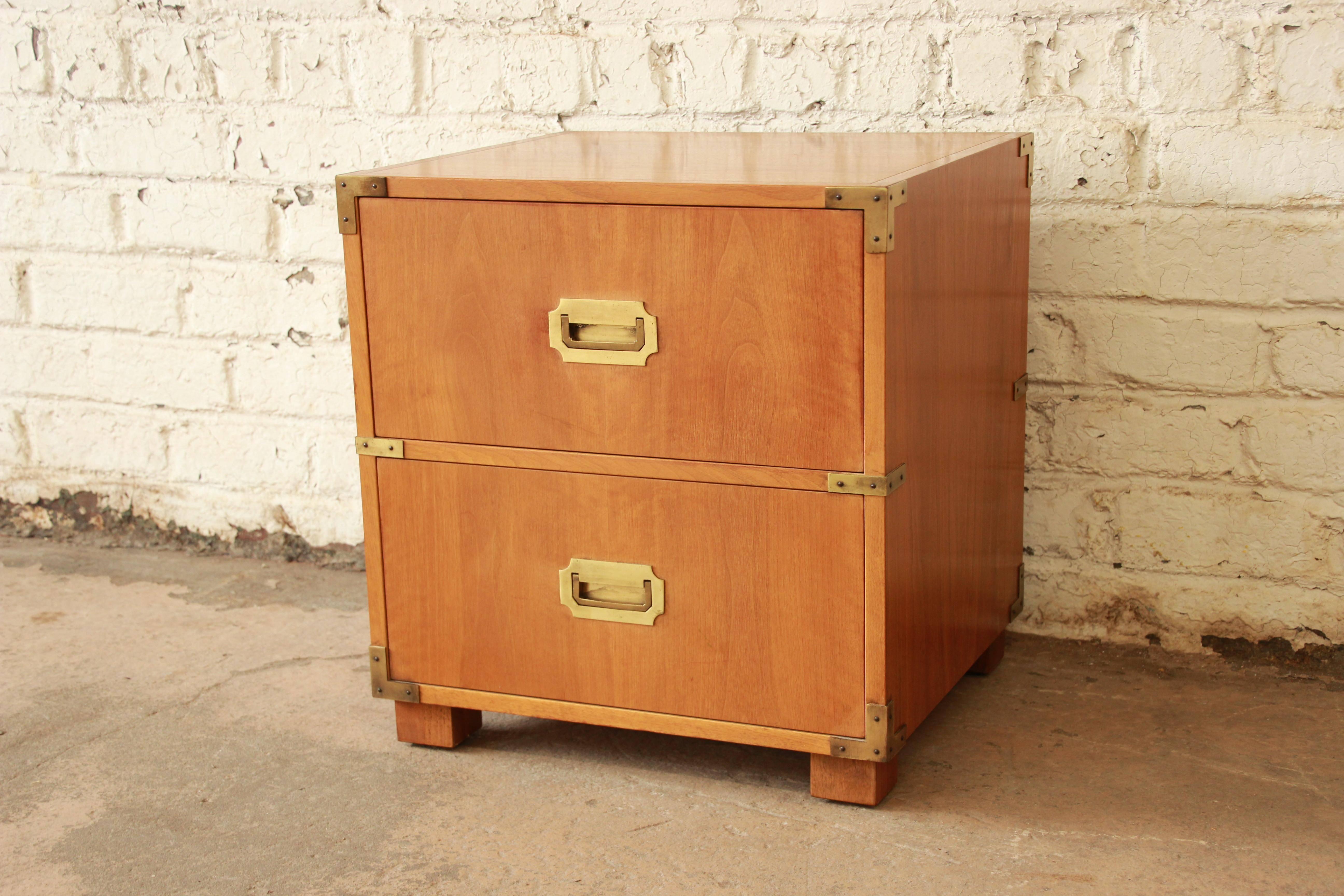 Gorgeous Mid-Century Campaign style nightstand or small chest by Baker Furniture Company. The chest features stunning bleached walnut wood grain and quality brass hardware. It offers good storage with a drop-front storage compartment and a deep