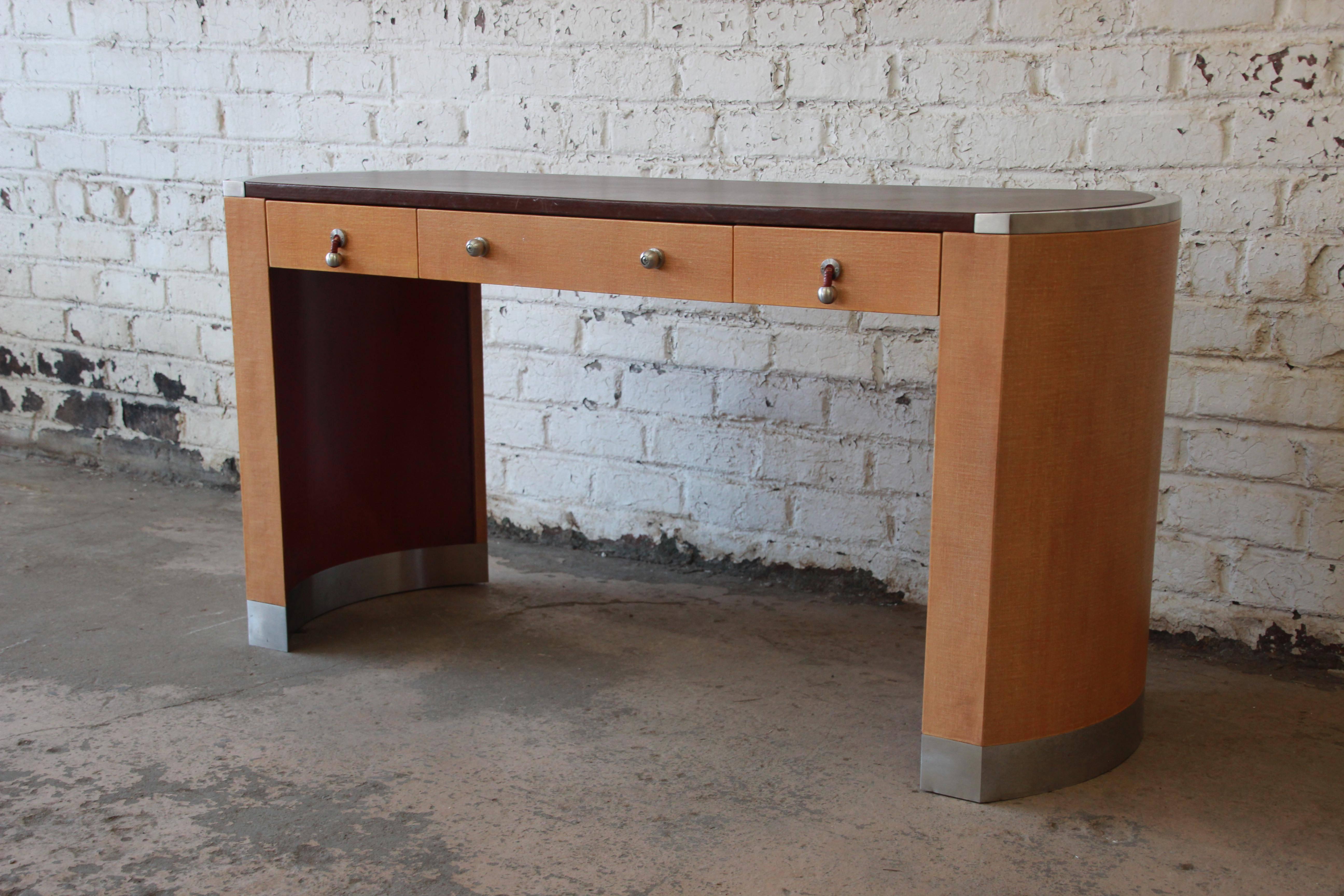 An exceptional modern Art Deco style desk designed by David Easton for Henredon. The desk features a nice brown leather writing surface, banded chrome edges at the top and bottom, and curved linen sides. It has three drawers that open and close