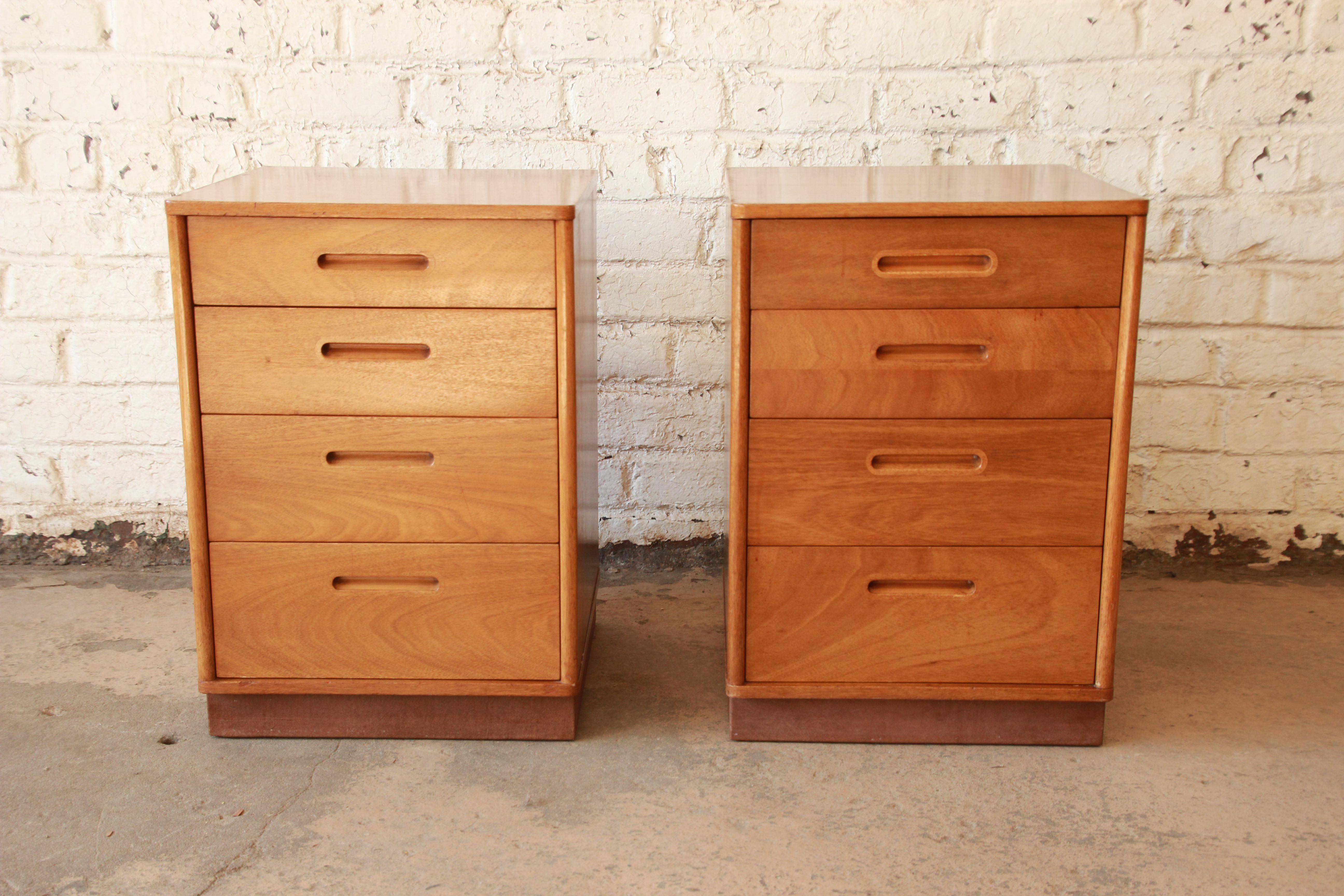 An exceptional pair of Mid-Century Modern mahogany nightstands or small chests designed by Edward Wormley for Dunbar. The nightstands feature gorgeous mahogany wood grain in an amber finish, a unique brown leather plinth base, and sleek Mid-Century