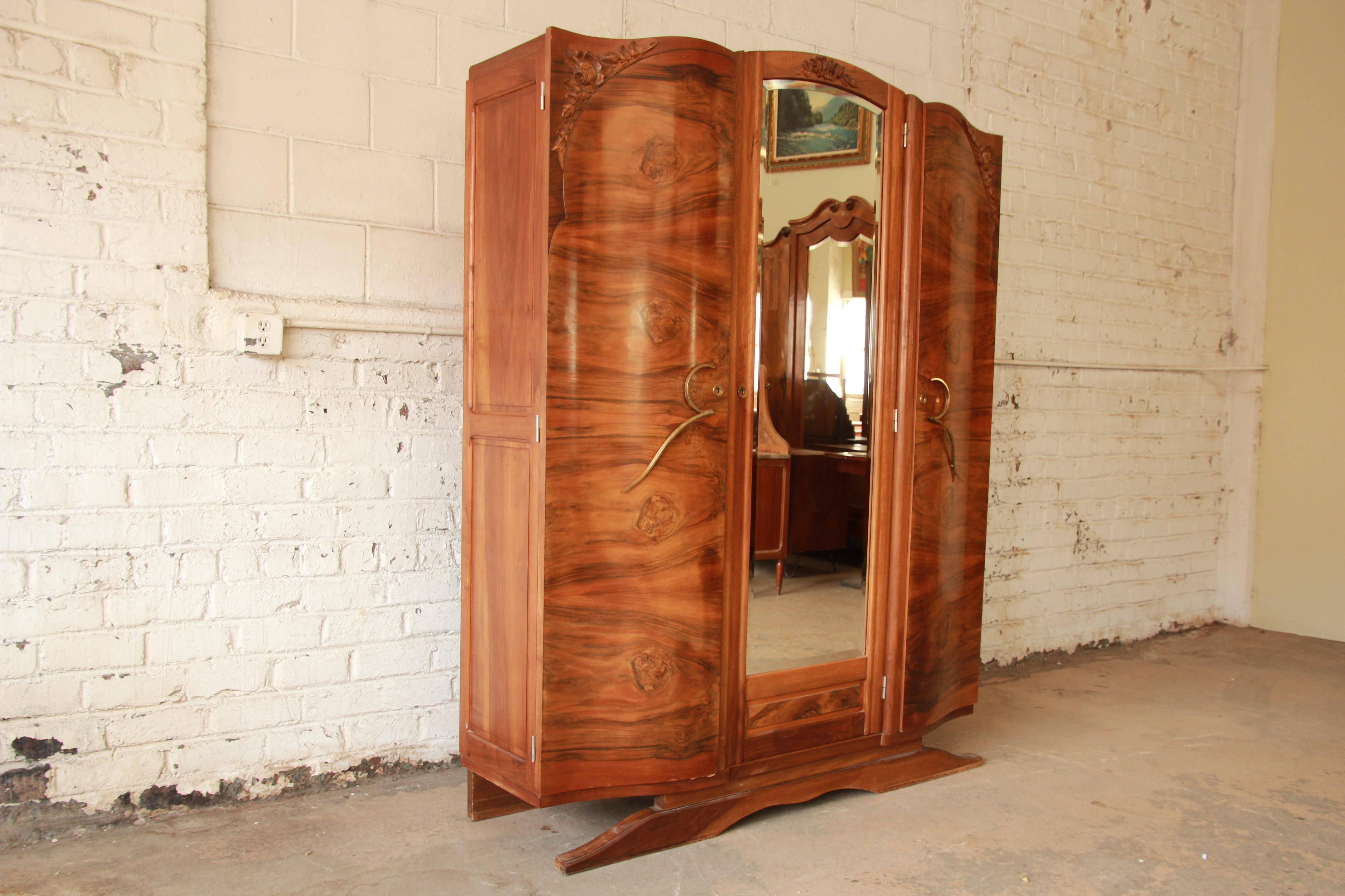 Exceptional 1930s French Art Deco knockdown wardrobe. The wardrobe features stunning burl wood grain, hand-carved details and a large beveled mirror. It offers ample room for storage, with open shelving throughout and a single dovetailed drawer. The