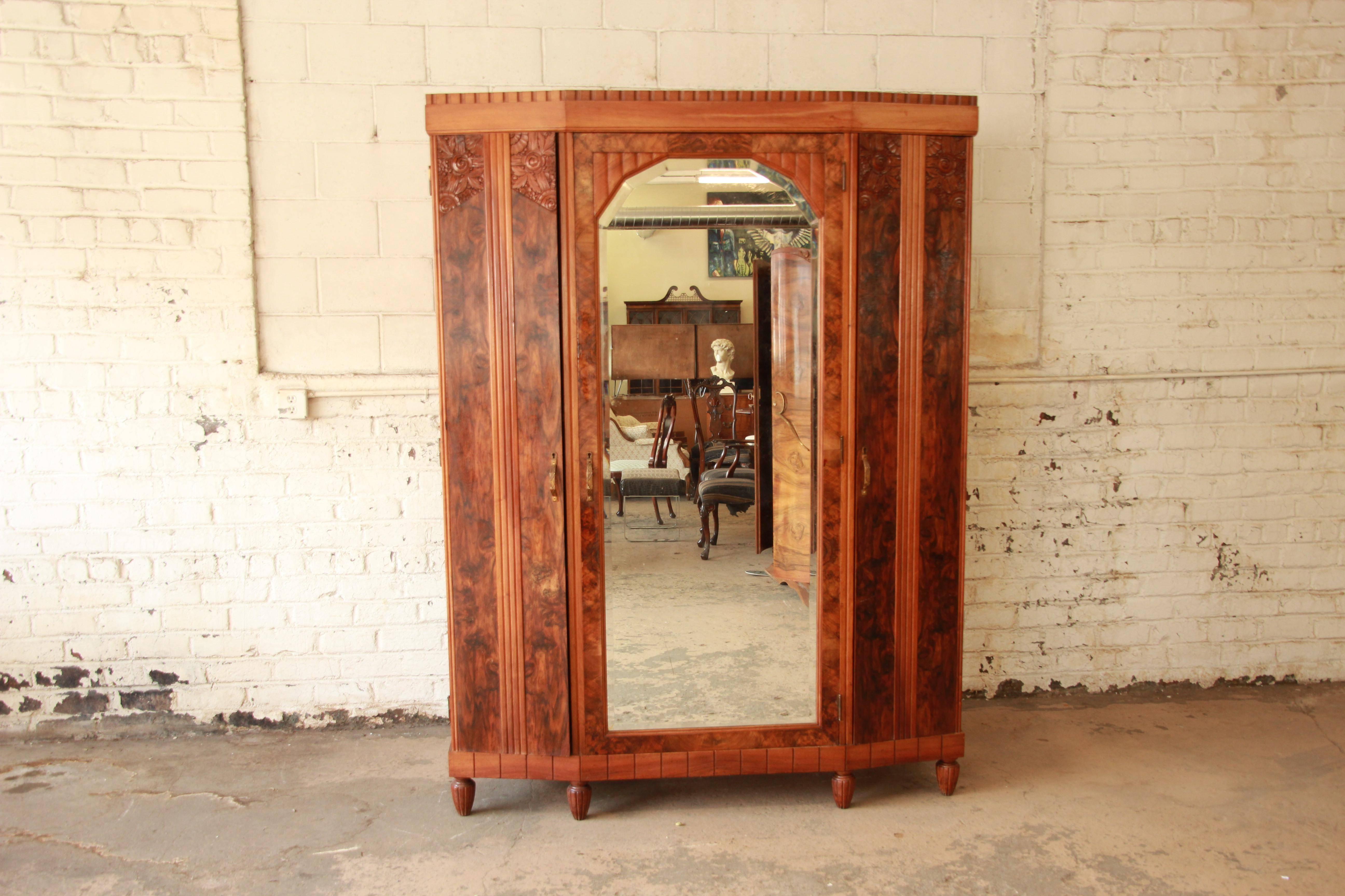 Exceptional 1930s French Art Deco knockdown wardrobe. The wardrobe features stunning burl wood grain, hand-carved details, and a large beveled mirror. It offers ample room for storage, with open shelving throughout and two dovetailed drawers. The