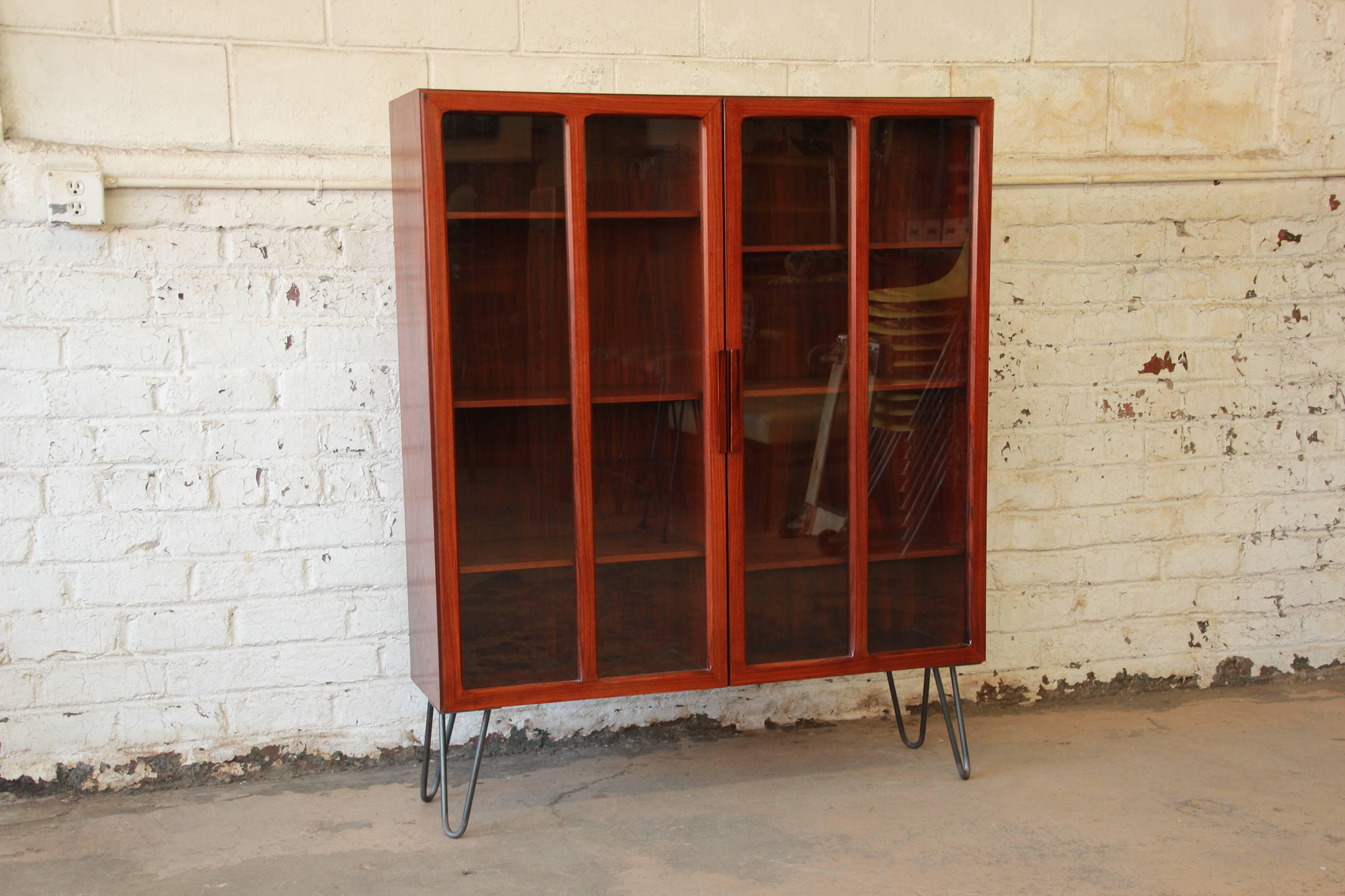 Danish Modern rosewood glass front bookcase or display cabinet designed by Ib Kofod Larsen for Faarup Møbelfabrik, circa 1960s. The bookcase features stunning wood grain and clean, sleek Mid-Century lines. The case rests on stylish metal hairpin