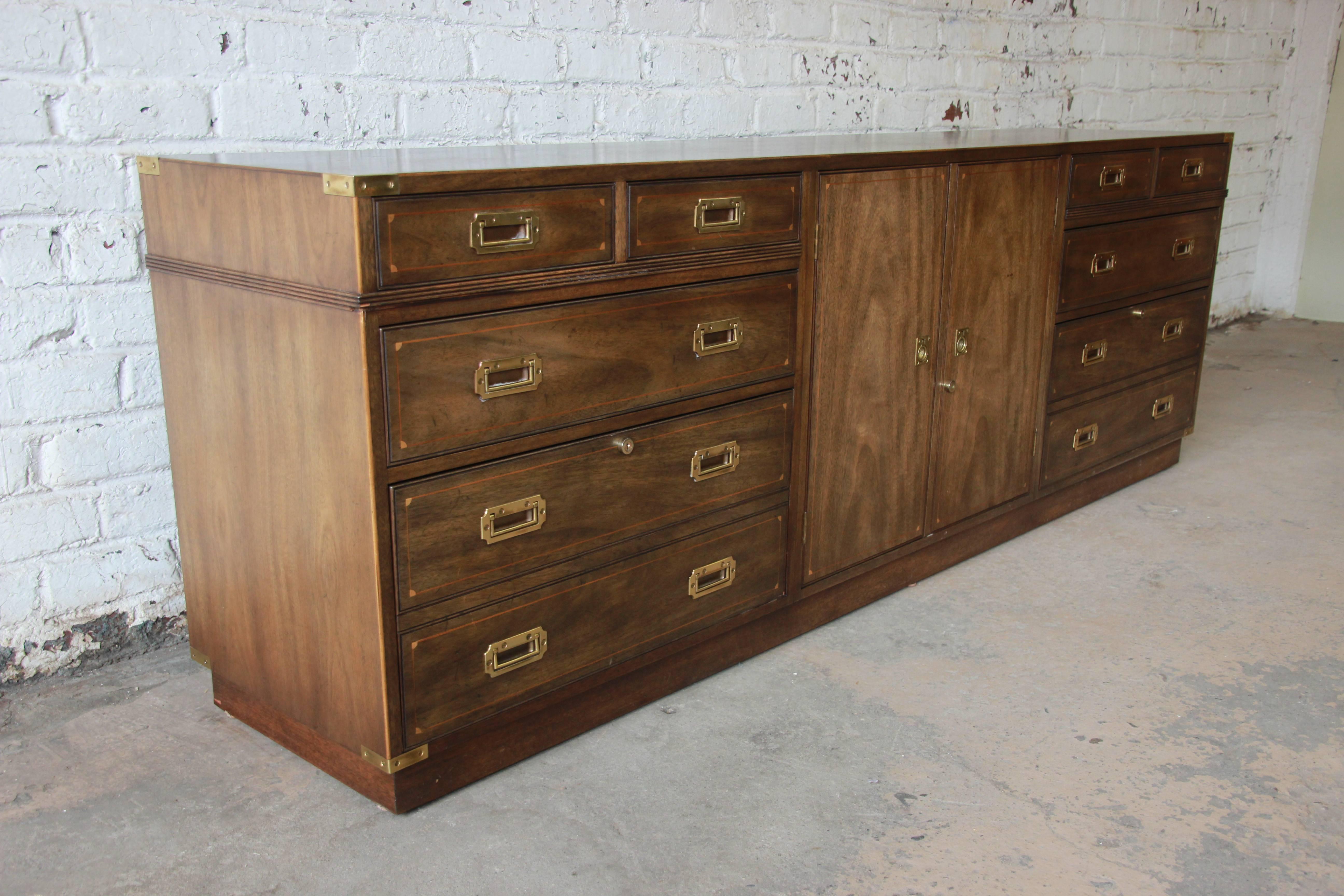 Stunning vintage Kittinger campaign credenza. The credenza has brass hardware with inlaid details. It features eight drawers, two with locking double hanging file organizers. The centre cabinet opens up to an adjustable shelf that locks along with