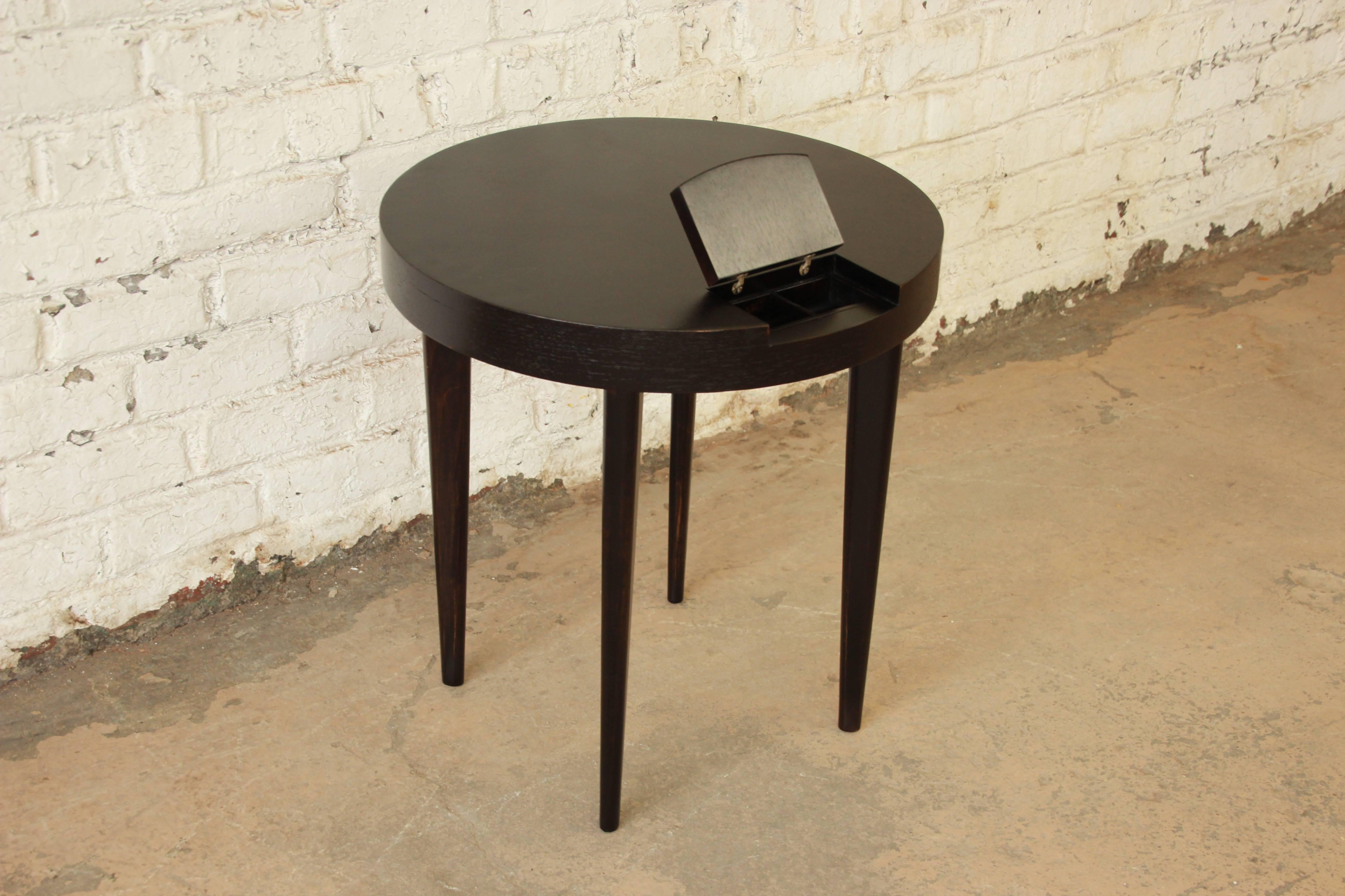 Exceptional Mid-Century ebonized round occasional table by iconic designer Gilbert Rohde for Herman Miller. The table features sleek, Minimalist lines and a beautiful ebonized finish. It has a unique hidden flip-up storage compartment. The table has