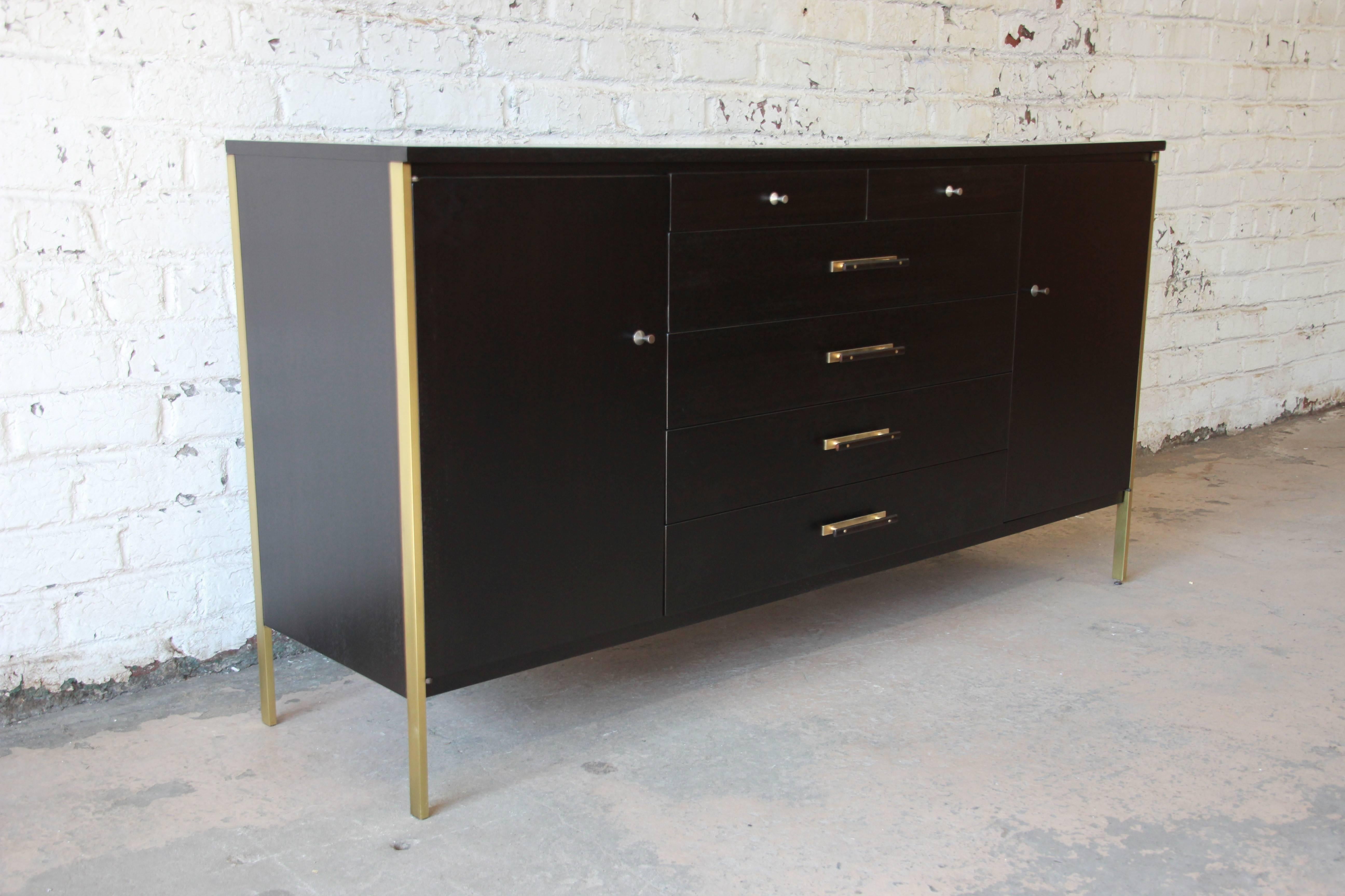 Mid-Century Modern ebonized walnut credenza by Paul McCobb for Calvin Furniture. This credenza has been fully restored with polished brass and original pulls. Six center drawers are flanked by two cabinets with adjustable shelves. The lower shelves