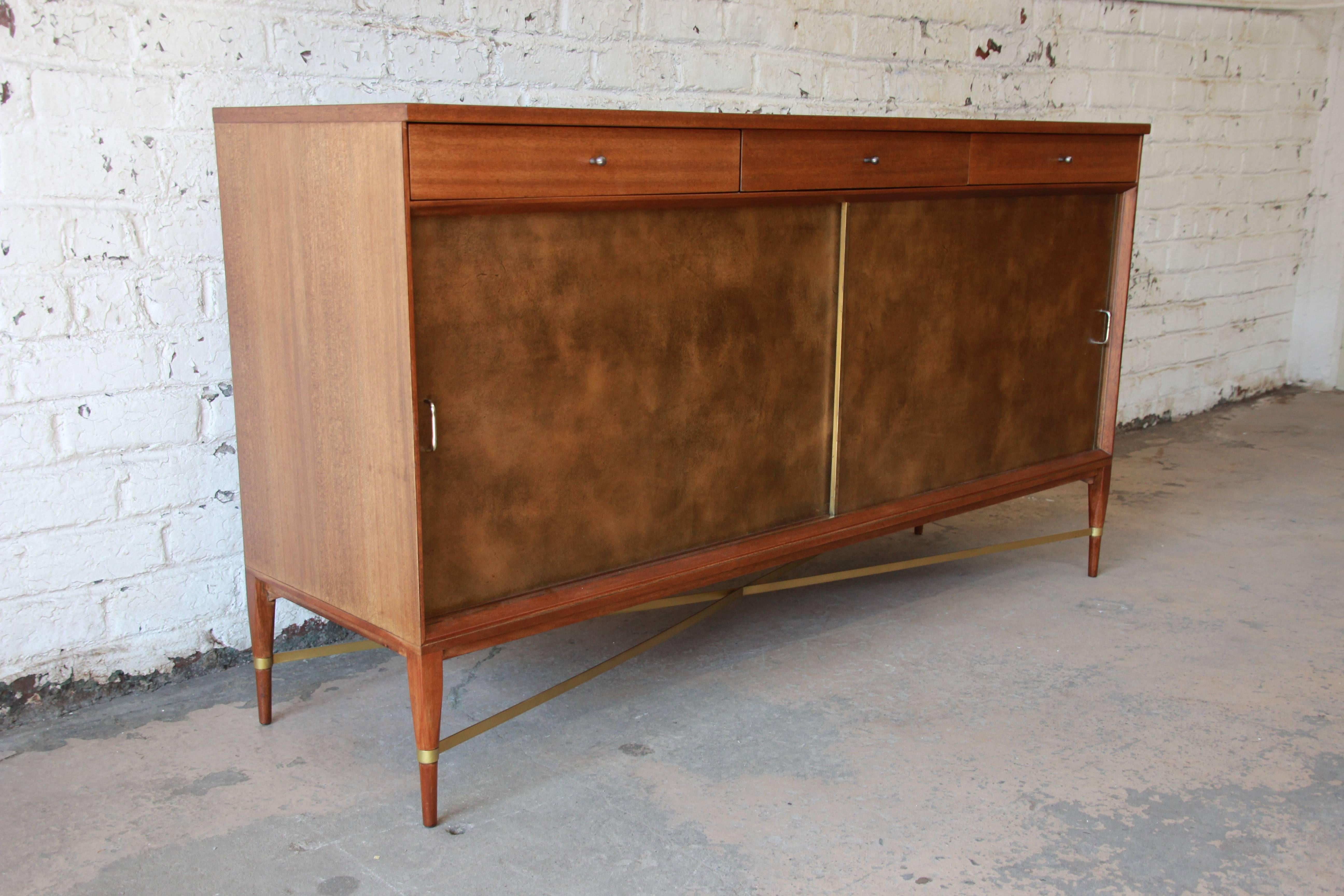 Paul McCobb credenza or sideboard for Calvin Furniture, Connoisseur Collection. The piece has two leather front sliding cabinet doors with brass pulls. Inside are two adjustable shelves for storage. Above are three drawers with original pulls. The