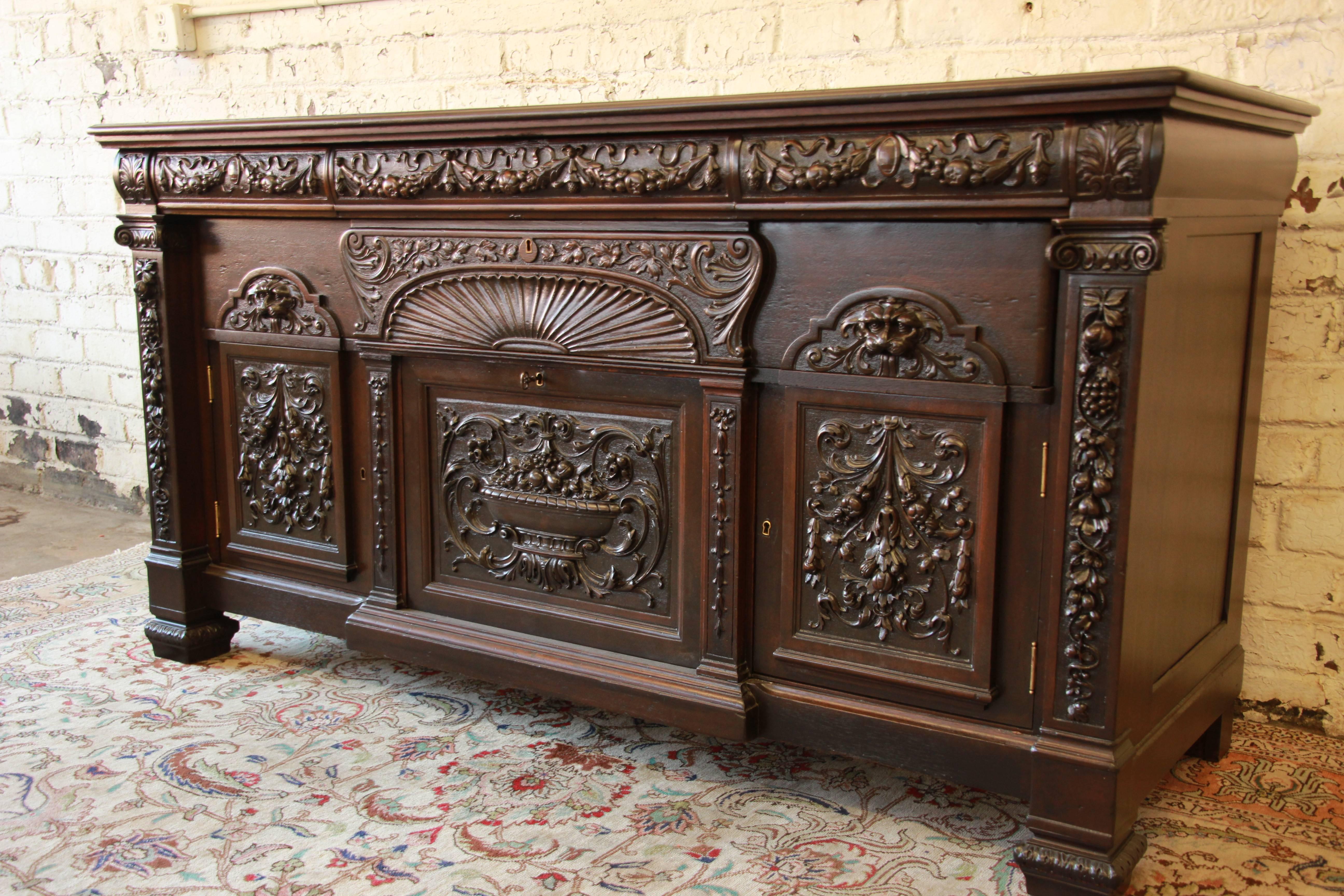 A beautiful 19th century ornately carved mahogany Victorian sideboard in the manner of R.J. Horner. The sideboard features stunning carved wood details, with a fruit basket motif. It offers ample room for storage, with three top drawers, a large
