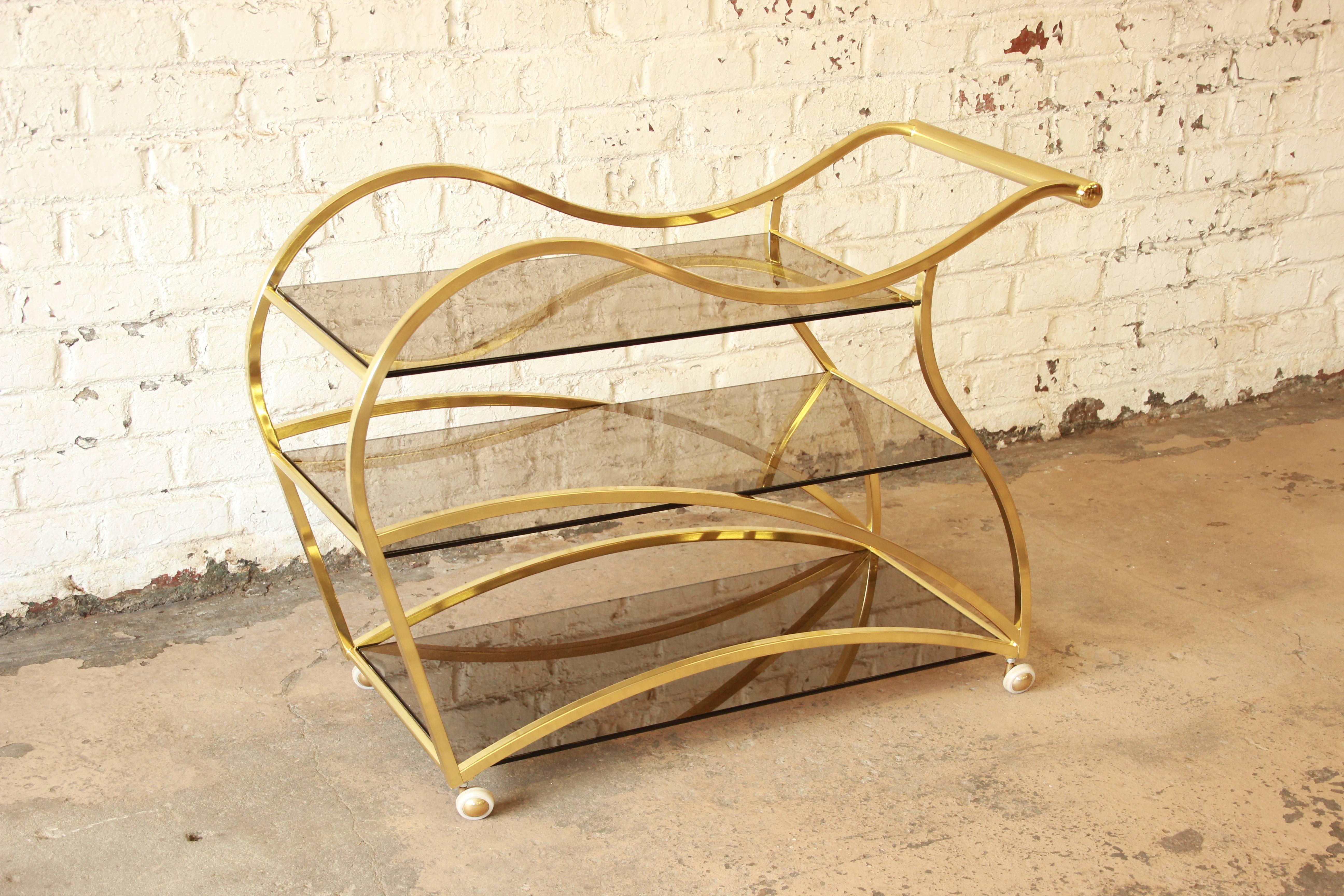A very rare curved brass and smoked glass bar cart attributed to Milo Baughman for the Design Institute of America. Sleek and stylish modern design. The cart sits on metal casters for easy mobility. Very unique example of Baughman's iconic design