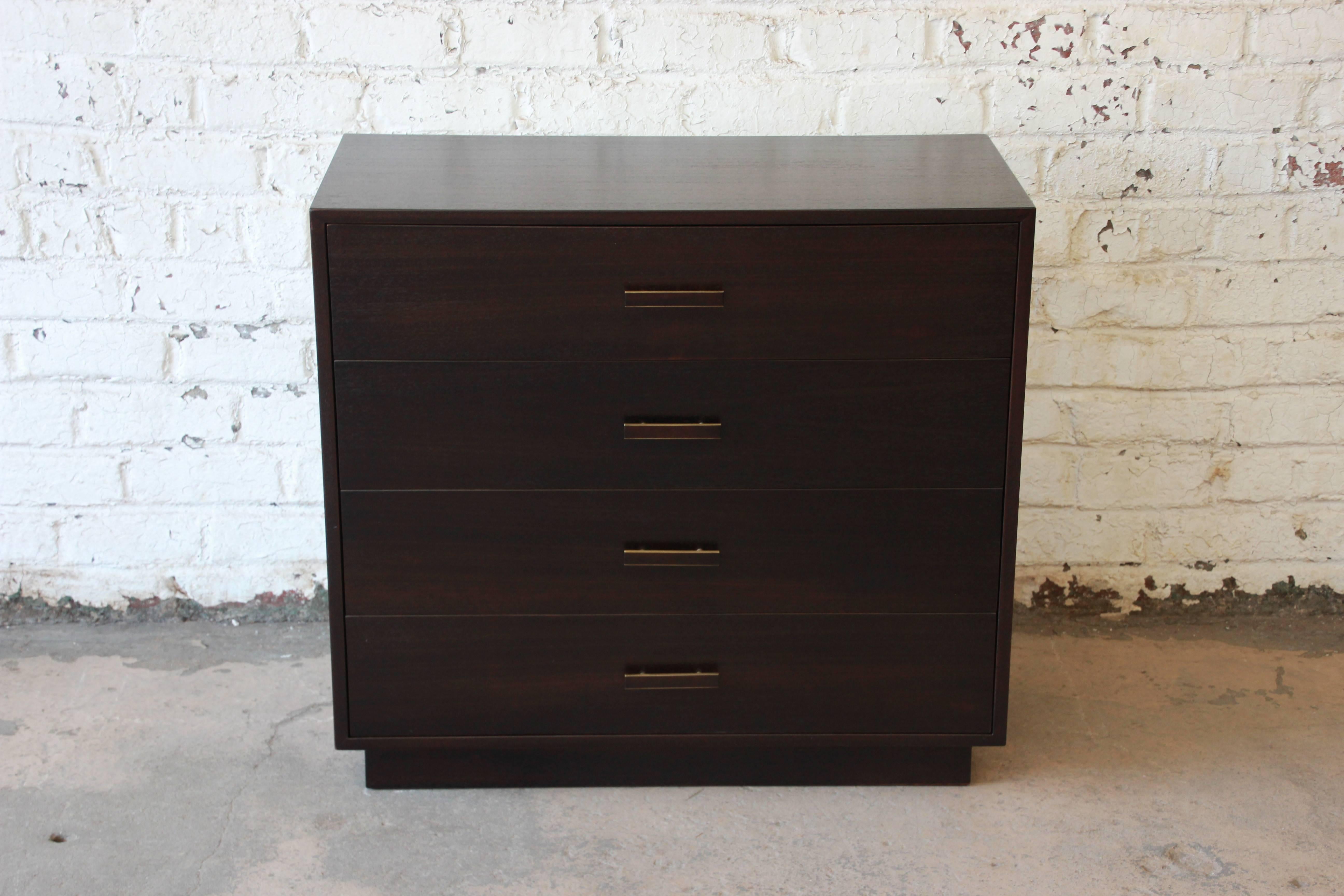 A stunning dark Mahogany and brass pulled gentlemen's chest by Harvey Probber. The chest has been restored and refinished in a dark mahogany. It offers four identical drawers with the top drawer offering dividers. The chest has a plinth base and