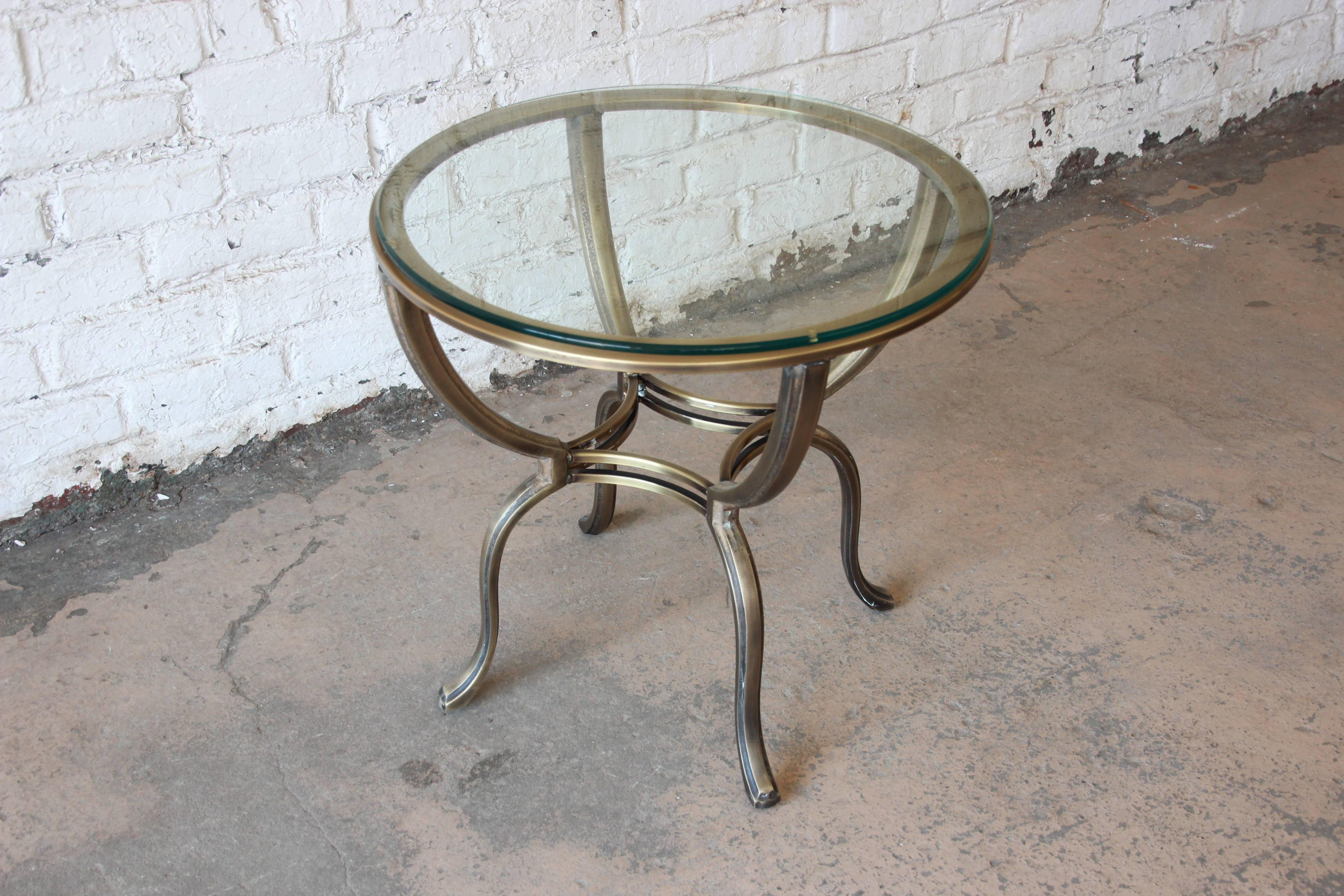 Beautiful solid brass round side table by Mastercraft. The table has a round bevelled edge glass top that sits upon four arms that form and elegant design. This piece is excellent vintage condition.