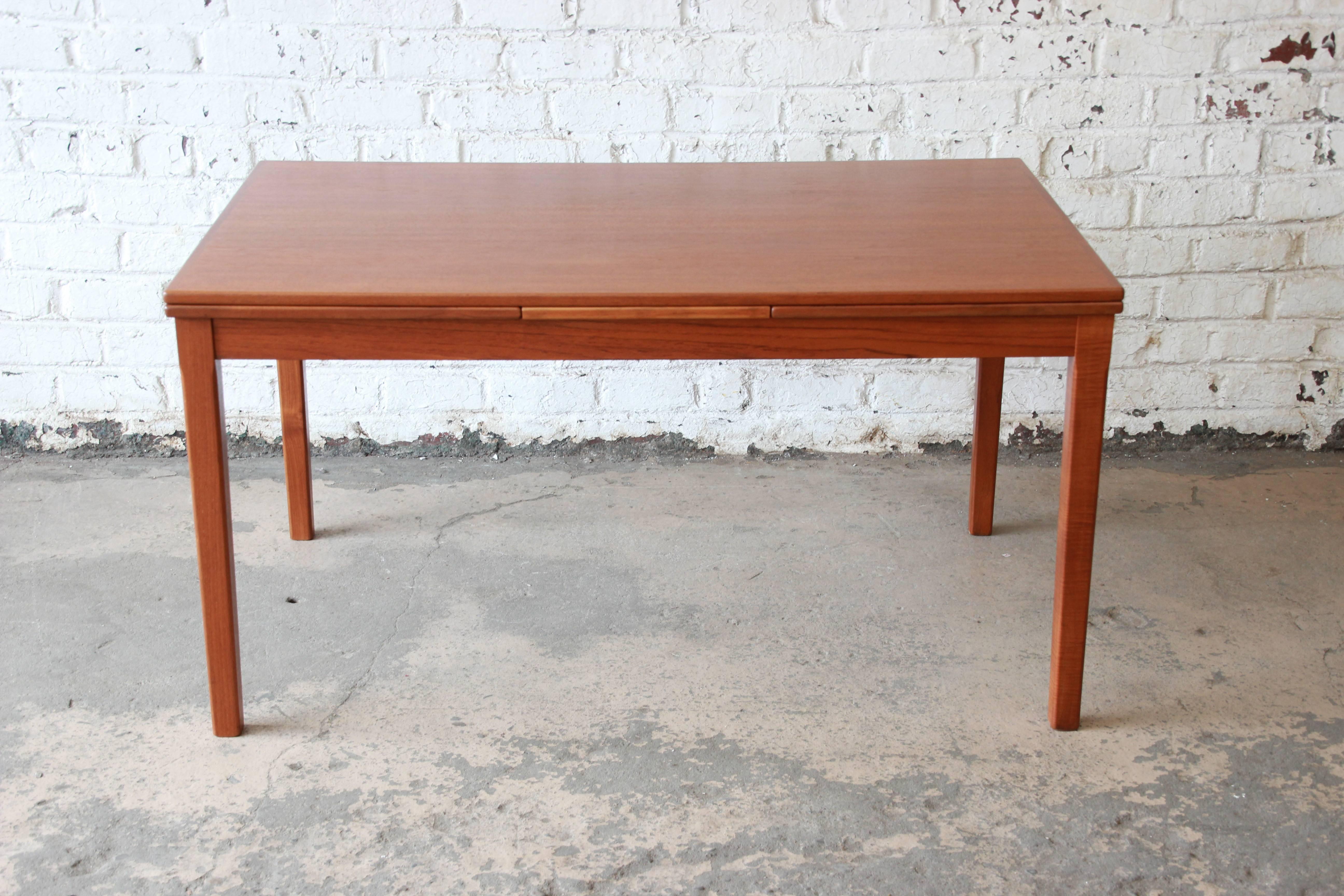 A beautiful 1960s Danish Modern teak draw leaf dining table in the style of Johannes Andersen for Uldum Møbelfabrik. The table features clean Mid-Century lines and gorgeous teak wood grain. It has been refinished and is in excellent condition.