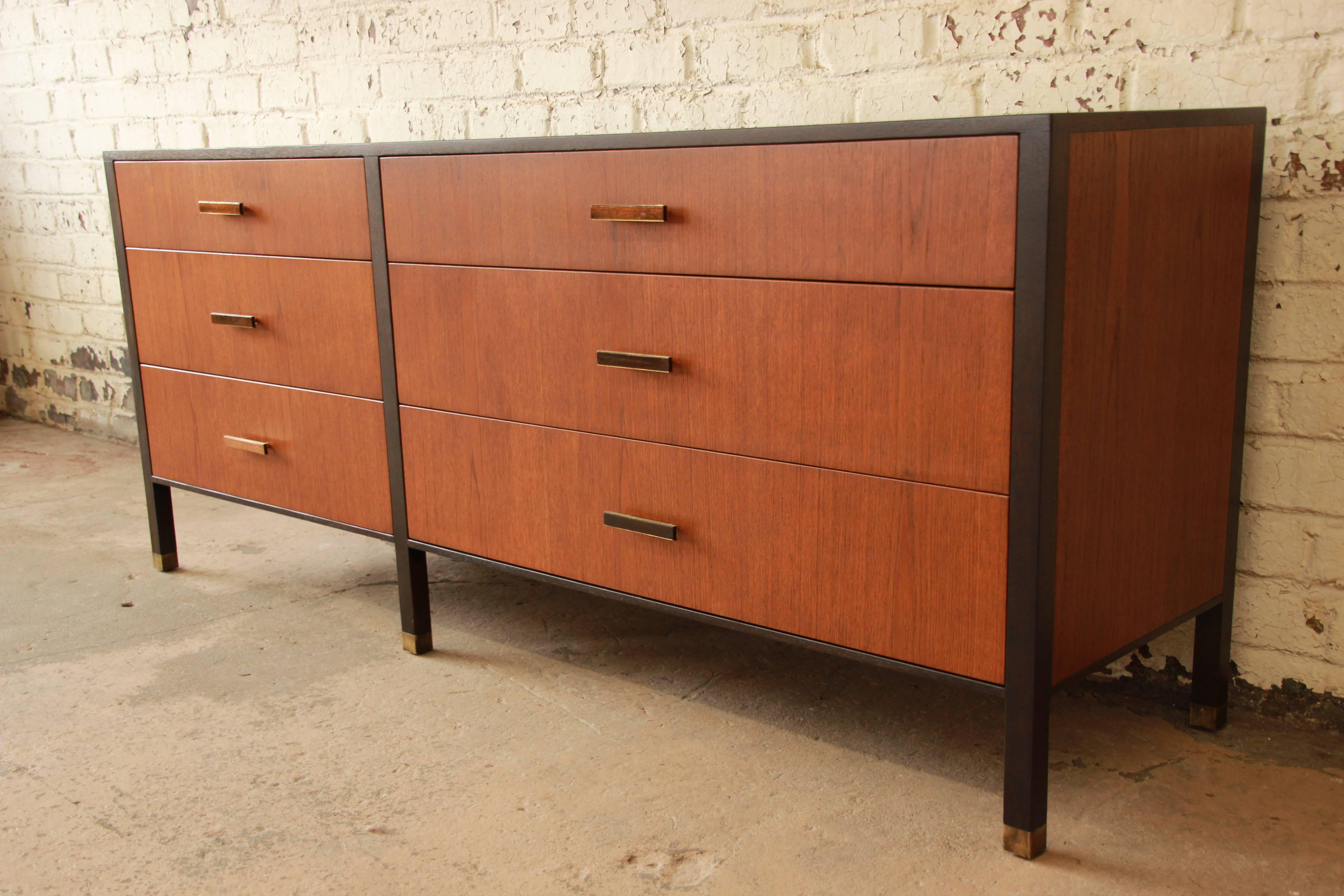 Offering an exceptional Mid-Century Modern six-drawer dresser or credenza designed by Harvey Probber. The dresser features beautiful walnut wood grain, with ebonized mahogany trim. It has brass tipped feet, as well as original brass and walnut