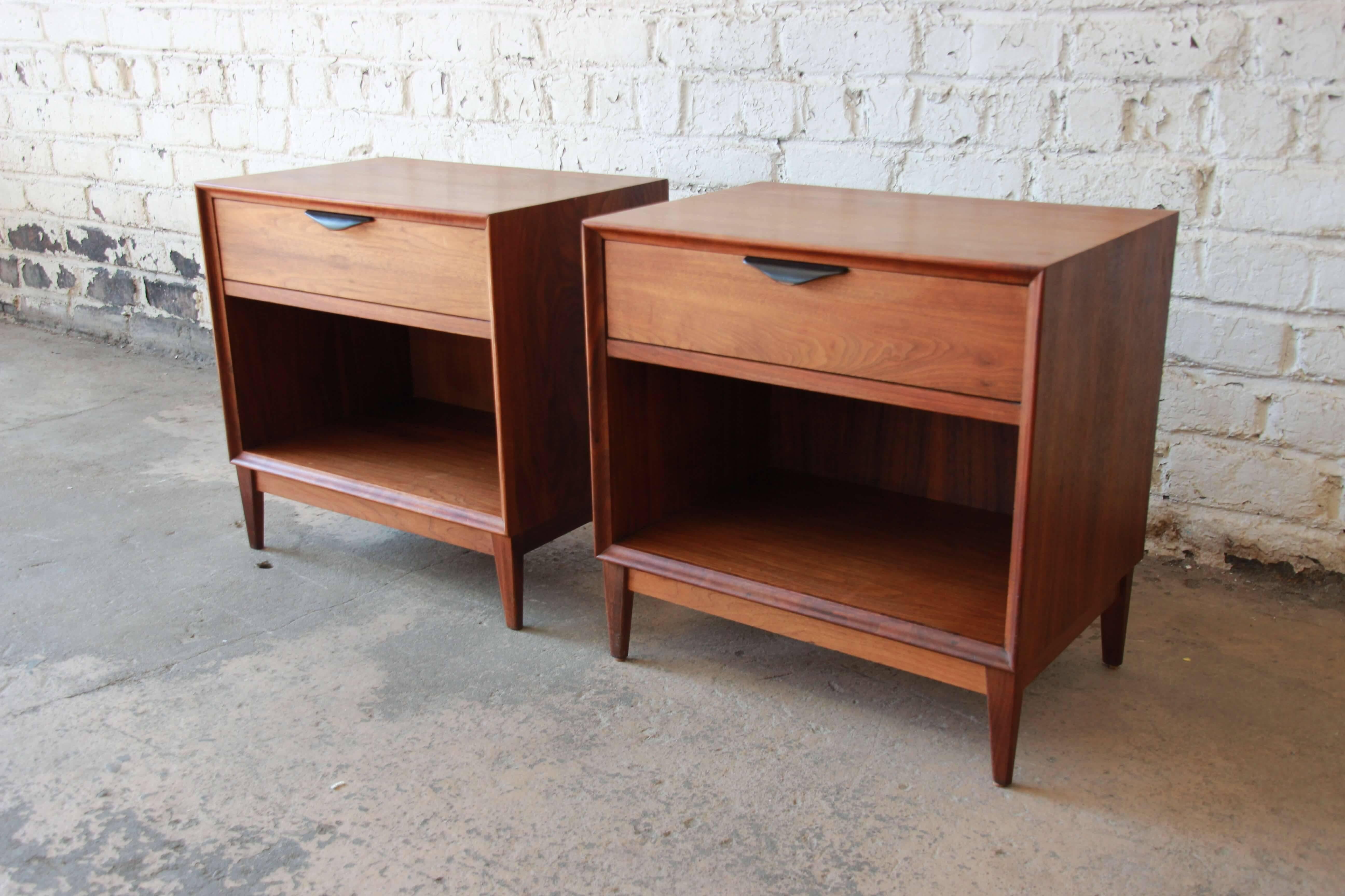 Offering a rare and exceptional pair of Mid-Century Modern nightstands by Dillingham. The pair of walnut nightstands have a Classic Mid-Century design with tapered legs leading up to a cabinet space for storage. The drawer has black lacquered pull