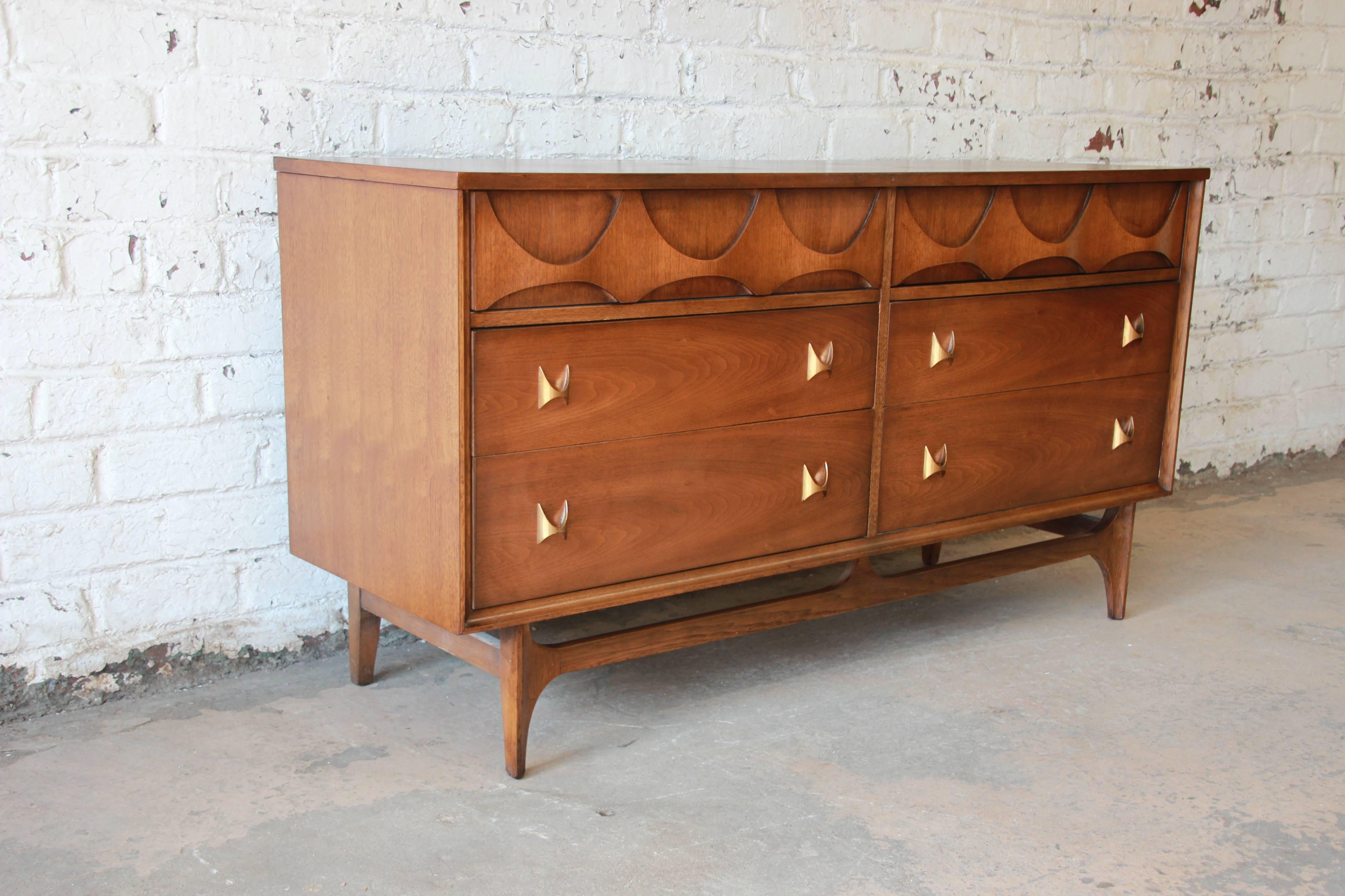 An exceptional Broyhill Brasilia six-drawer Mid-Century Modern sculpted walnut dresser or credenza. The dresser features gorgeous walnut wood grain, with sculpted arches and original pulls designed by Oscar Niemeyer. It offers ample room for storage