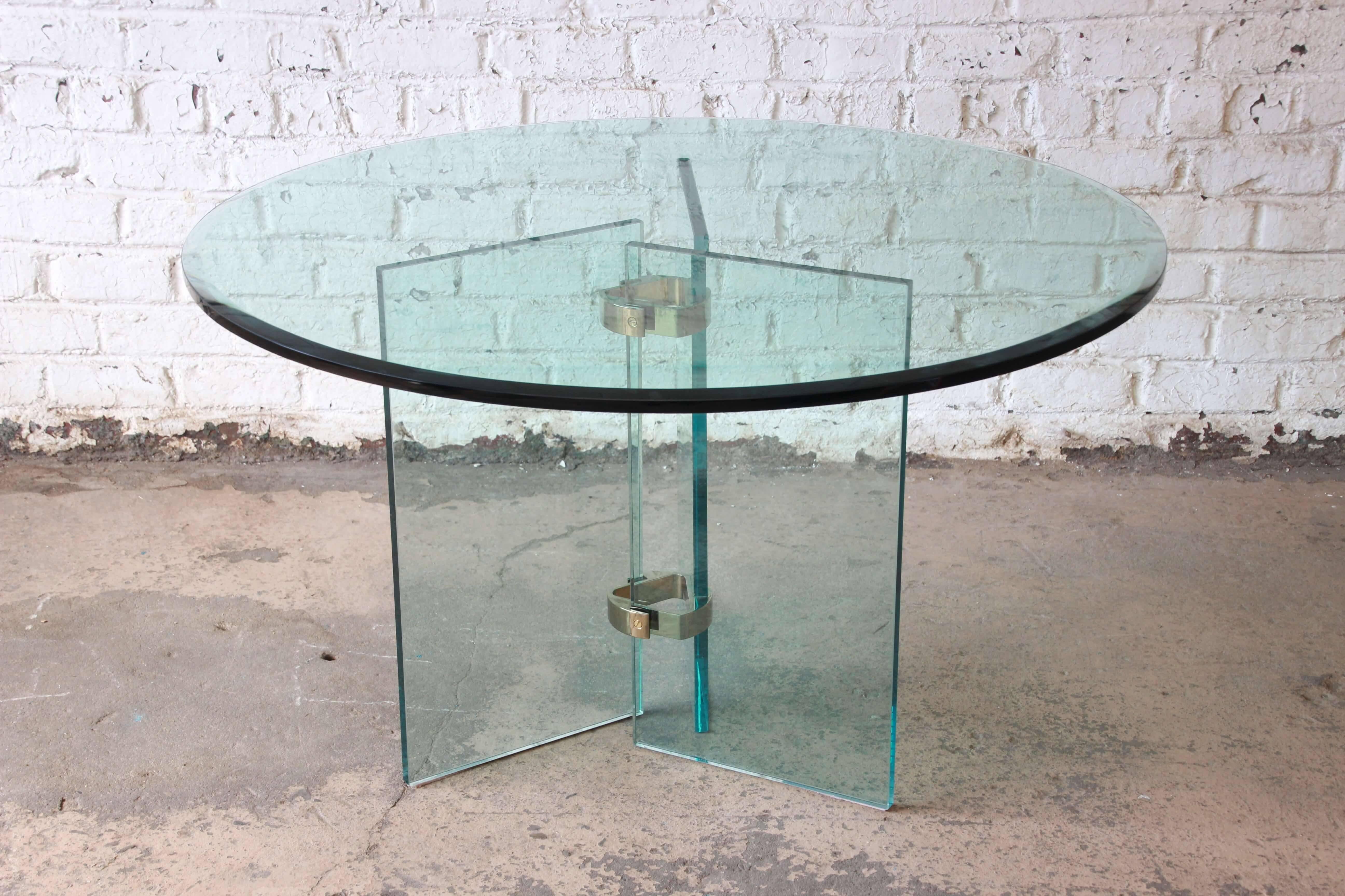 Offering a beautiful brass and glass round dining table in the style of Leon Rosen for Pace. It features a nice rounded beveled top that rests upon three sturdy glass legs. The legs have been fastened with polished brass brackets that give this