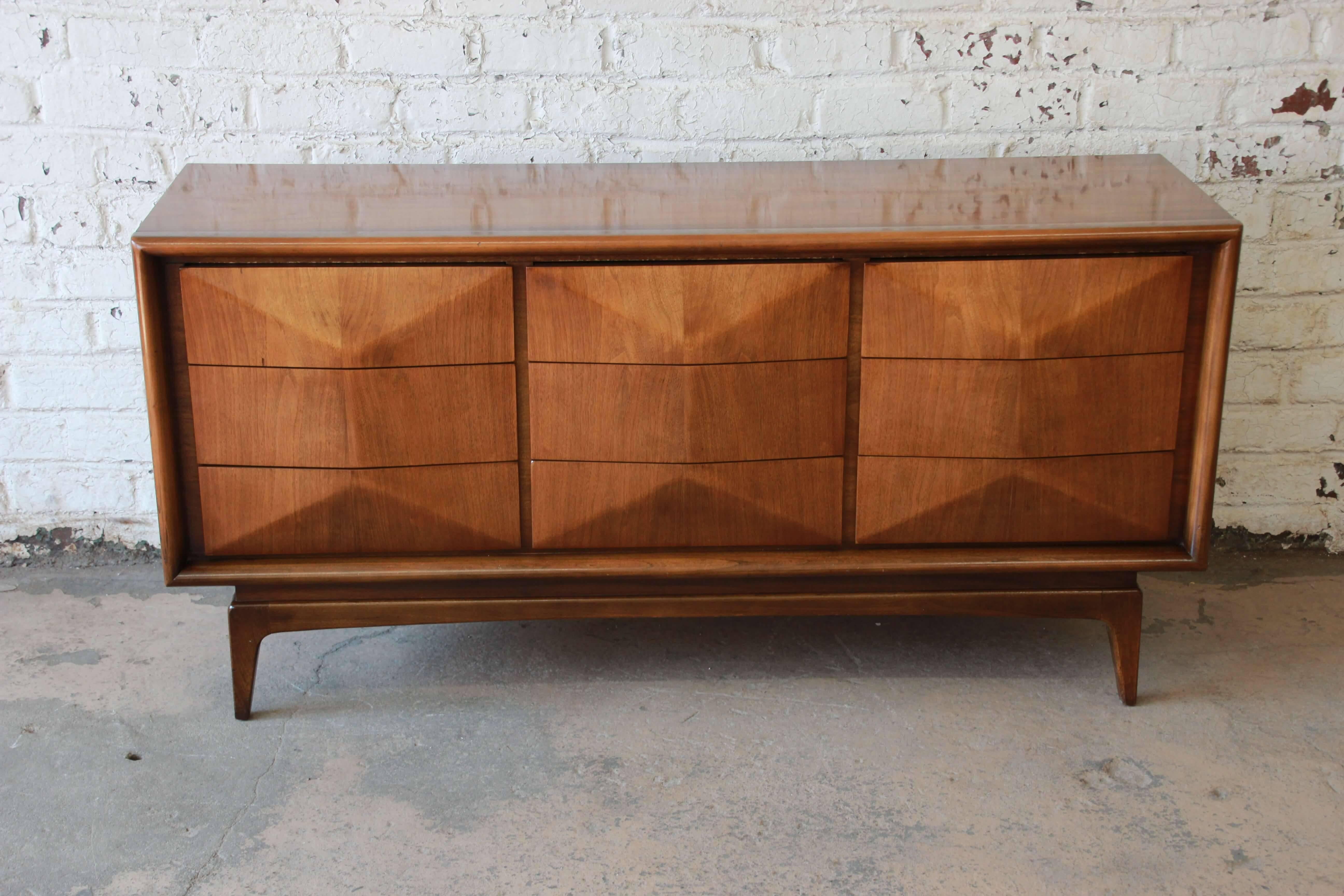 An exceptional and unique Mid-Century Modern diamond front dresser or credenza by United Furniture in the style of Vladimir Kagan. The dresser features stunning walnut wood grain and a sculpted diamond front with nine hefty drawers. It is well