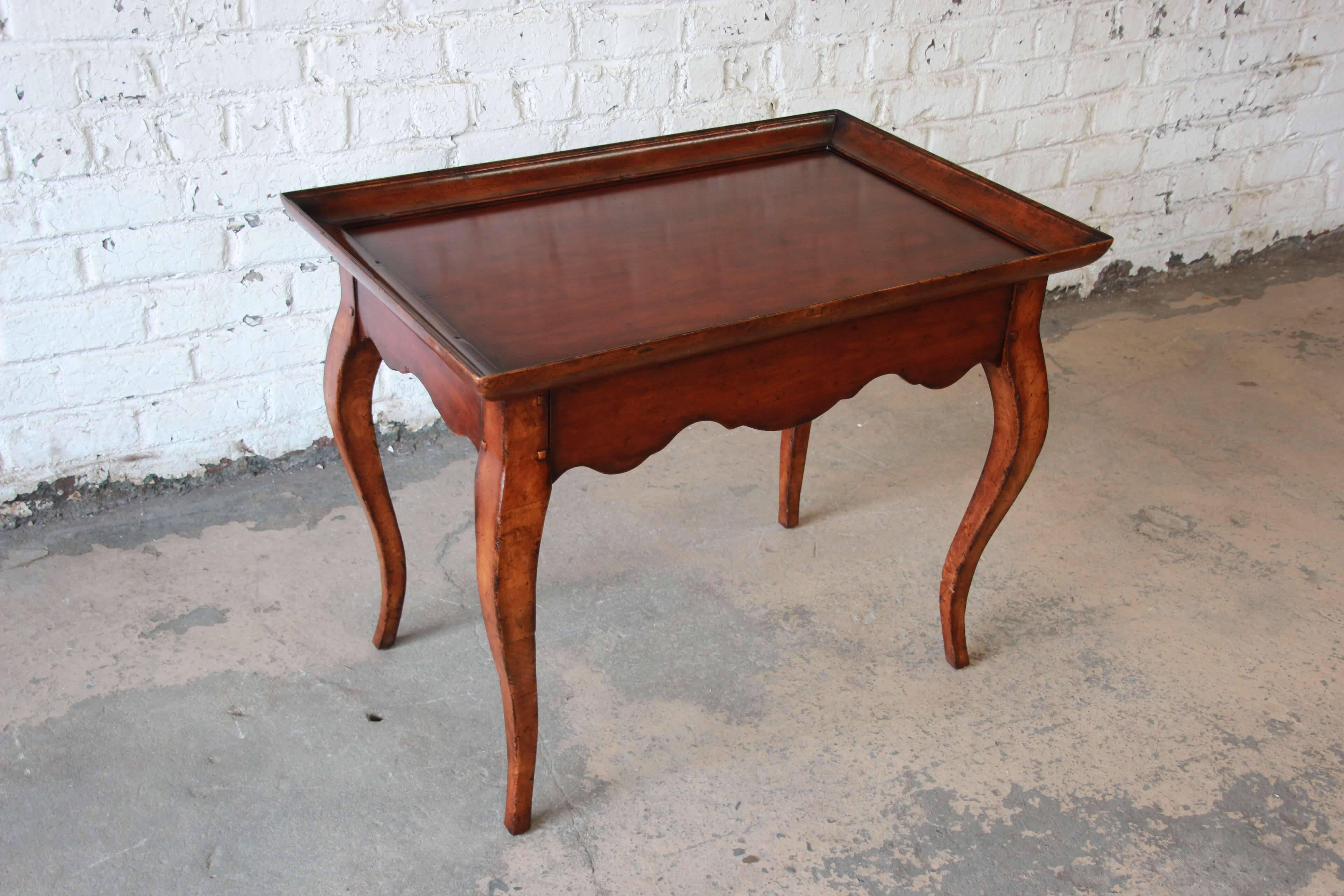 Offering a beautiful French side table by Ralph Lauren. The table has Provincial style legs and an antique design. The table is made from solid wood and has a nice sized surface with raised molded edging. Below there is a drawer for storage and