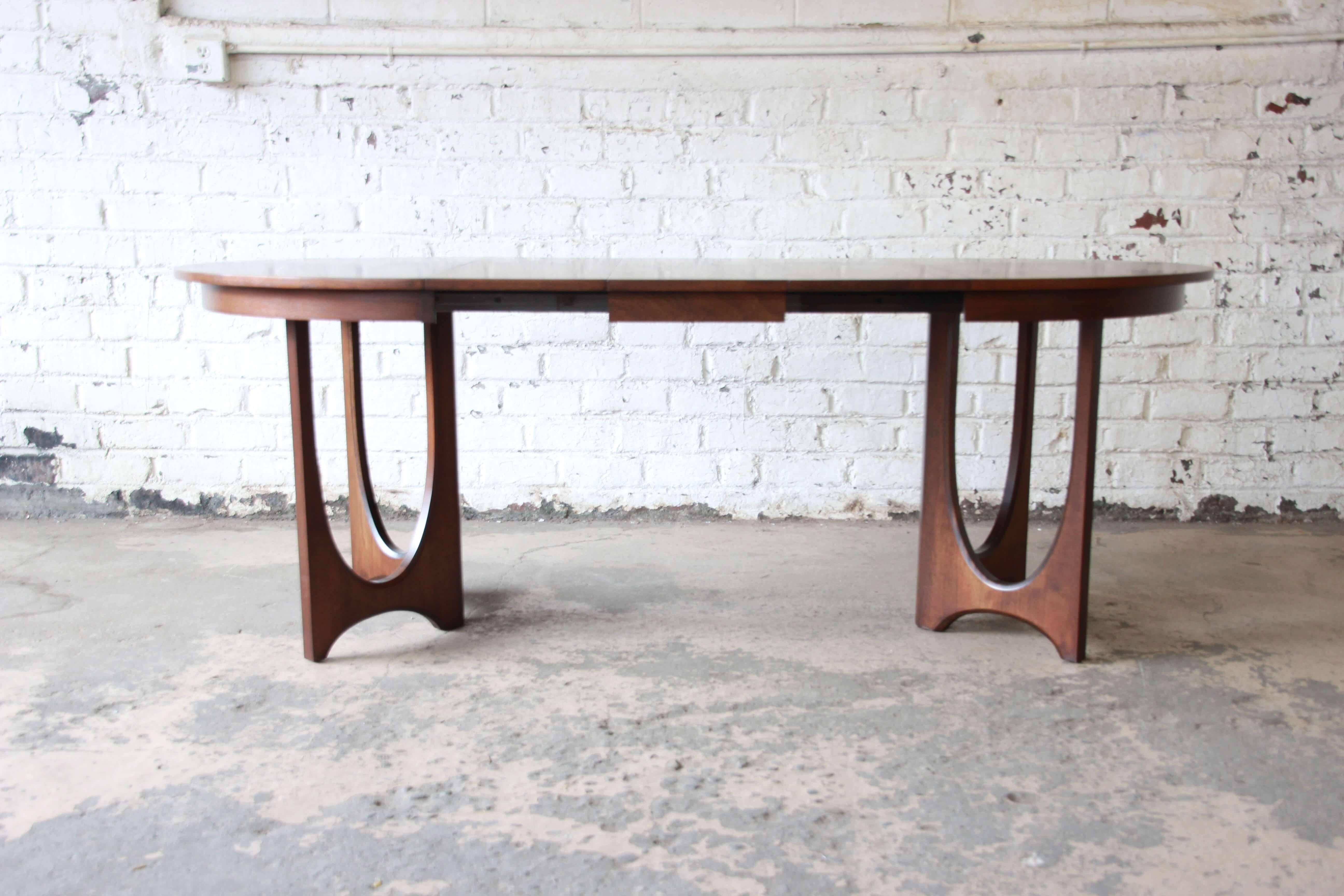 Offering a rare and amazing Broyhill Brasilia sculpted walnut dinging table. It sits on two sculpted arch bases. As a round table it makes a comfortable table for a small eating area or apartment. The table includes three leaves (12