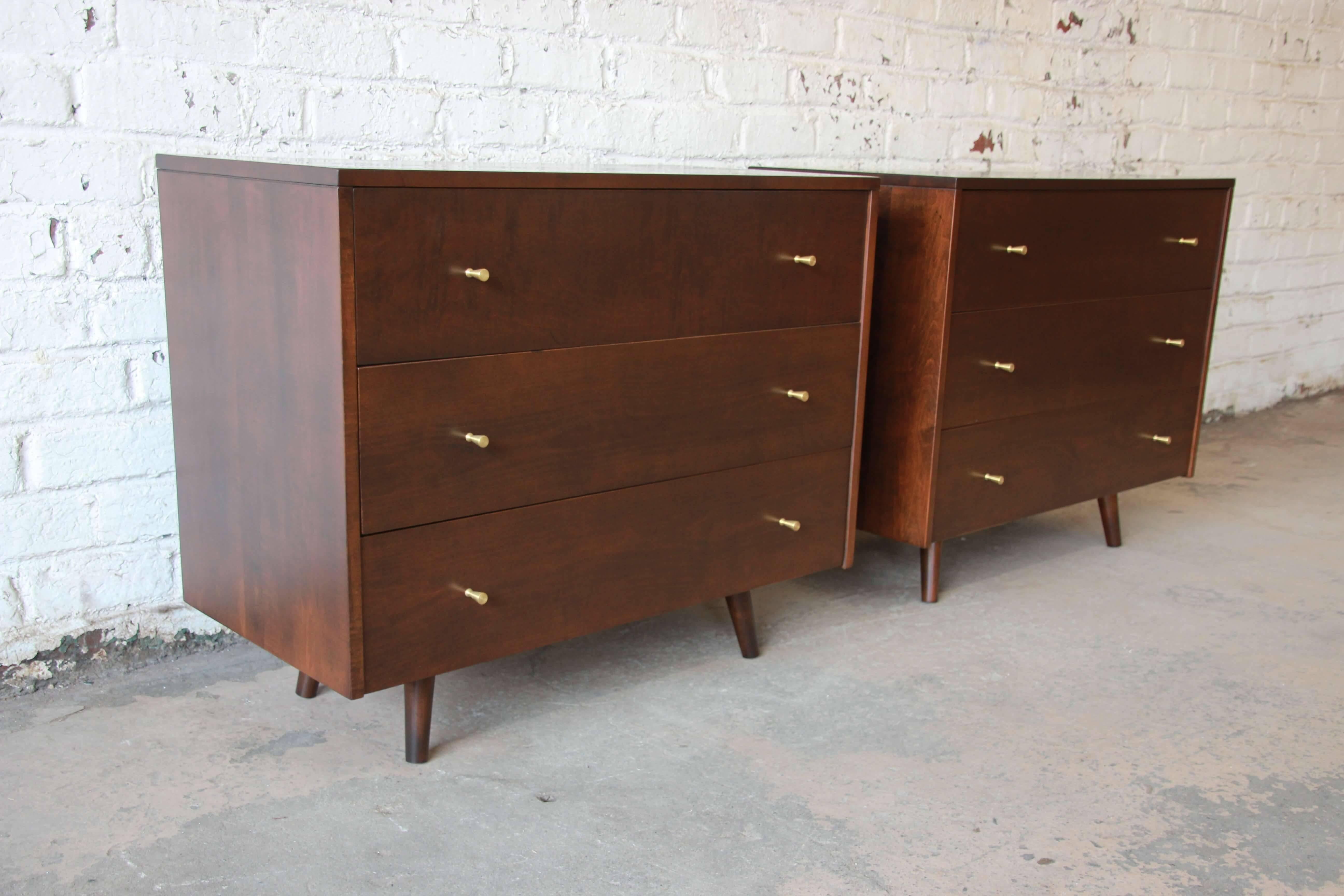 Offering a stunning pair of Paul McCobb three-drawer dressers. The pair have been restored in a medium brown walnut that is accented by brass pulls. Each drawer opens and closes smoothly while providing ample room for storage. Great set for many
