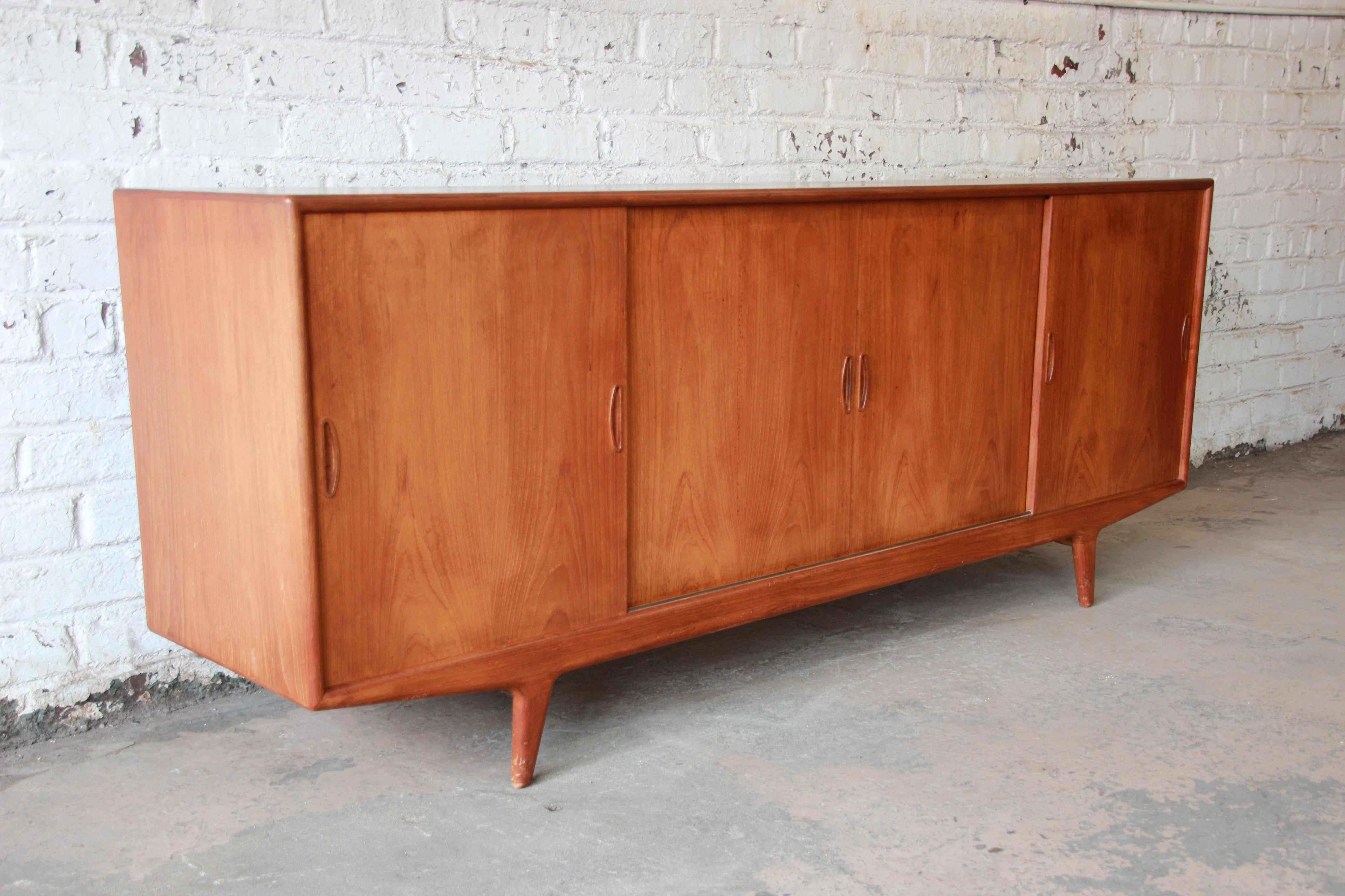 Offering an exceptional Mid-Century Danish Modern teak sideboard or credenza attributed to Arne Vodder. The credenza features stunning teakwood grain and unique splayed legs. It offers ample room for storage, with adjustable shelving on the left