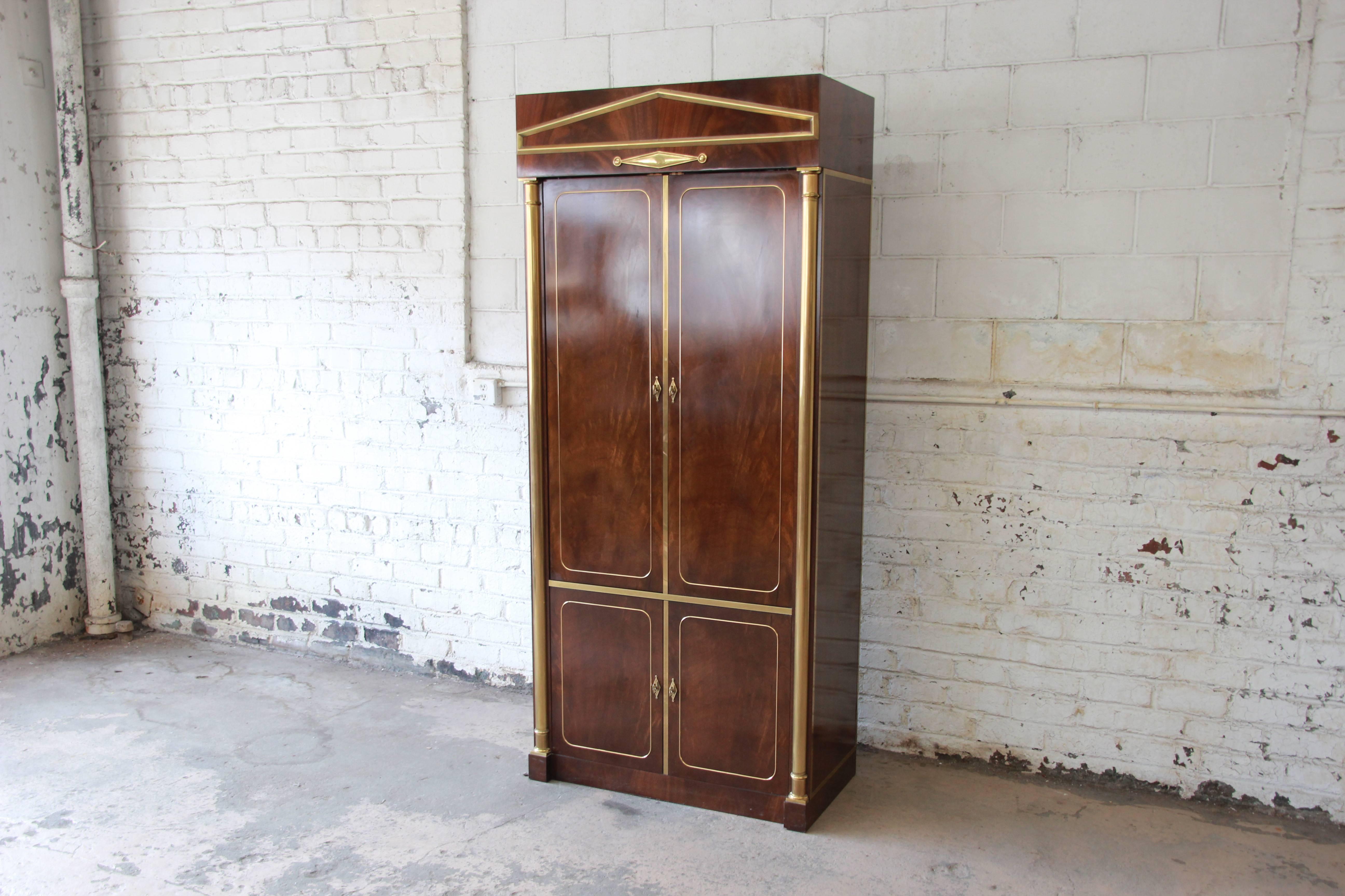 An exceptional burl wood and brass lighted bar cabinet by Mastercraft. The cabinet features stunning burl wood grain and handsome brass columns and trim. The top interior has a mirrored back, two glass shelves, a slide out tray, and a single