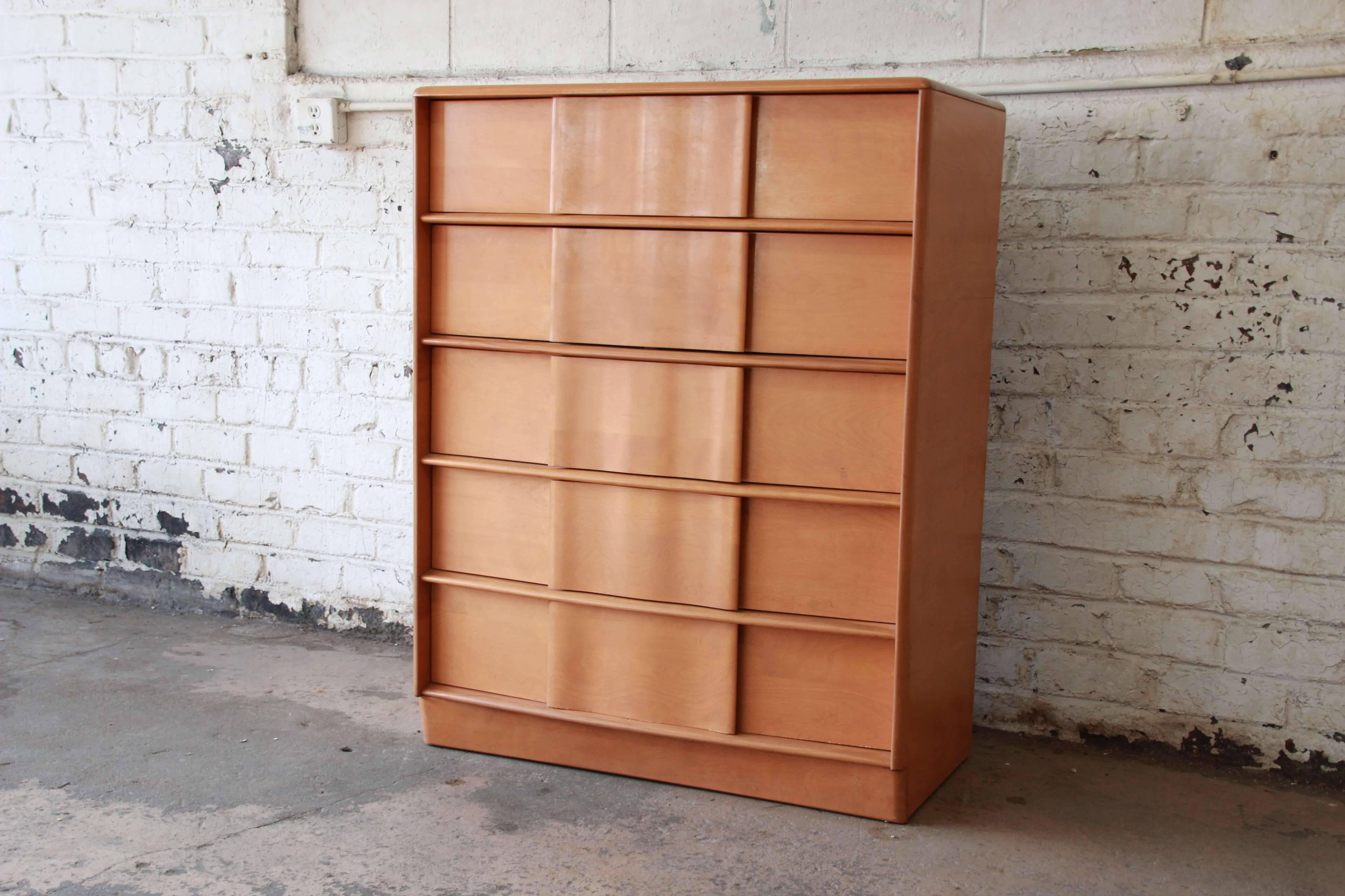 Offering a very nice Heywood-Wakefield Sculptura highboy dresser in champagne. This dresser has five smooth sliding drawers with sculpted pulls giving this a unique and defined modern style. It has a plinth base and is made from solid maple. The