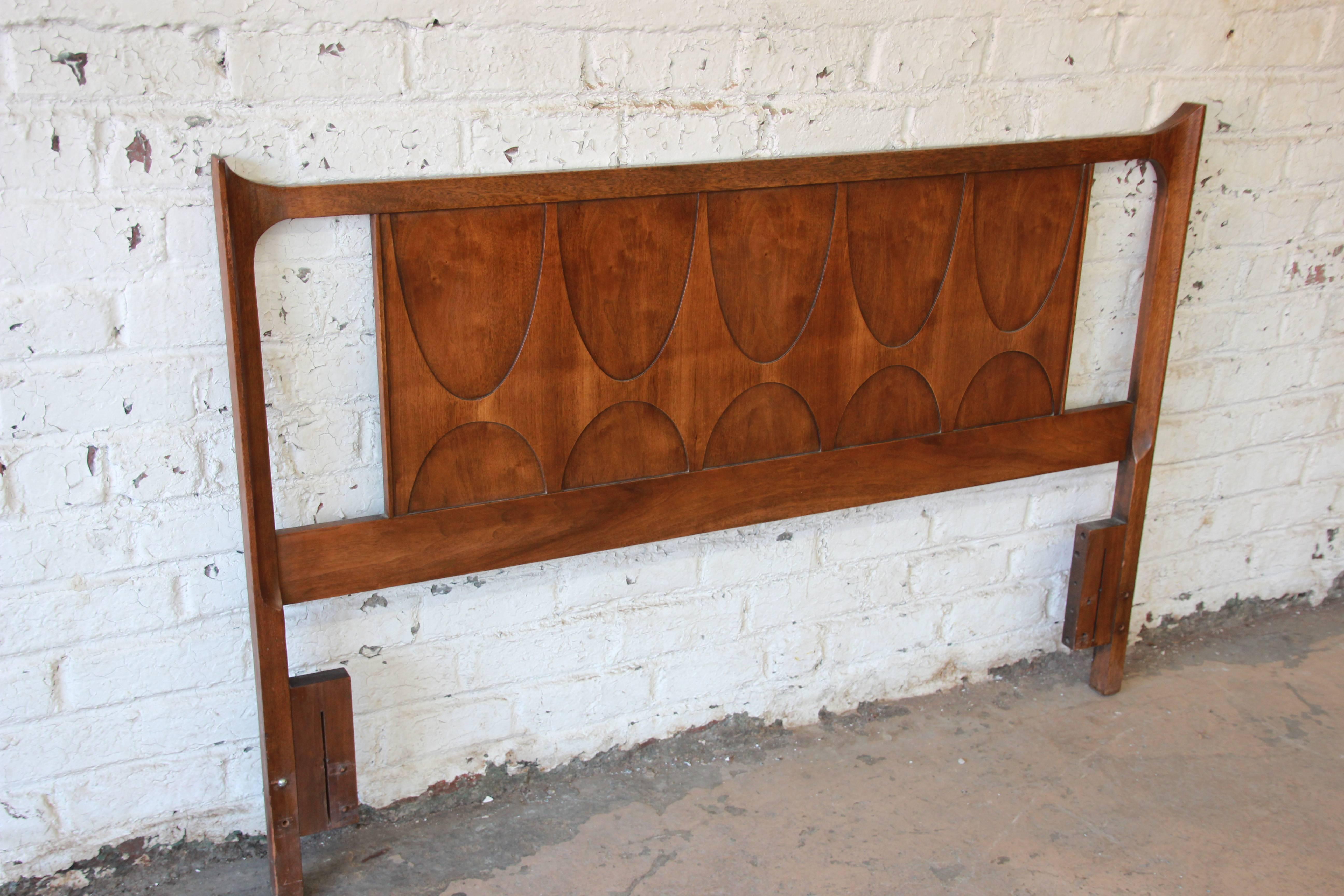 An exceptional Mid-Century Modern sculpted walnut queen or full size headboard by Broyhill Brasilia. The headboard features gorgeous walnut wood grain and classic Brasilia design. It was originally designed for both a queen and full bed. There are