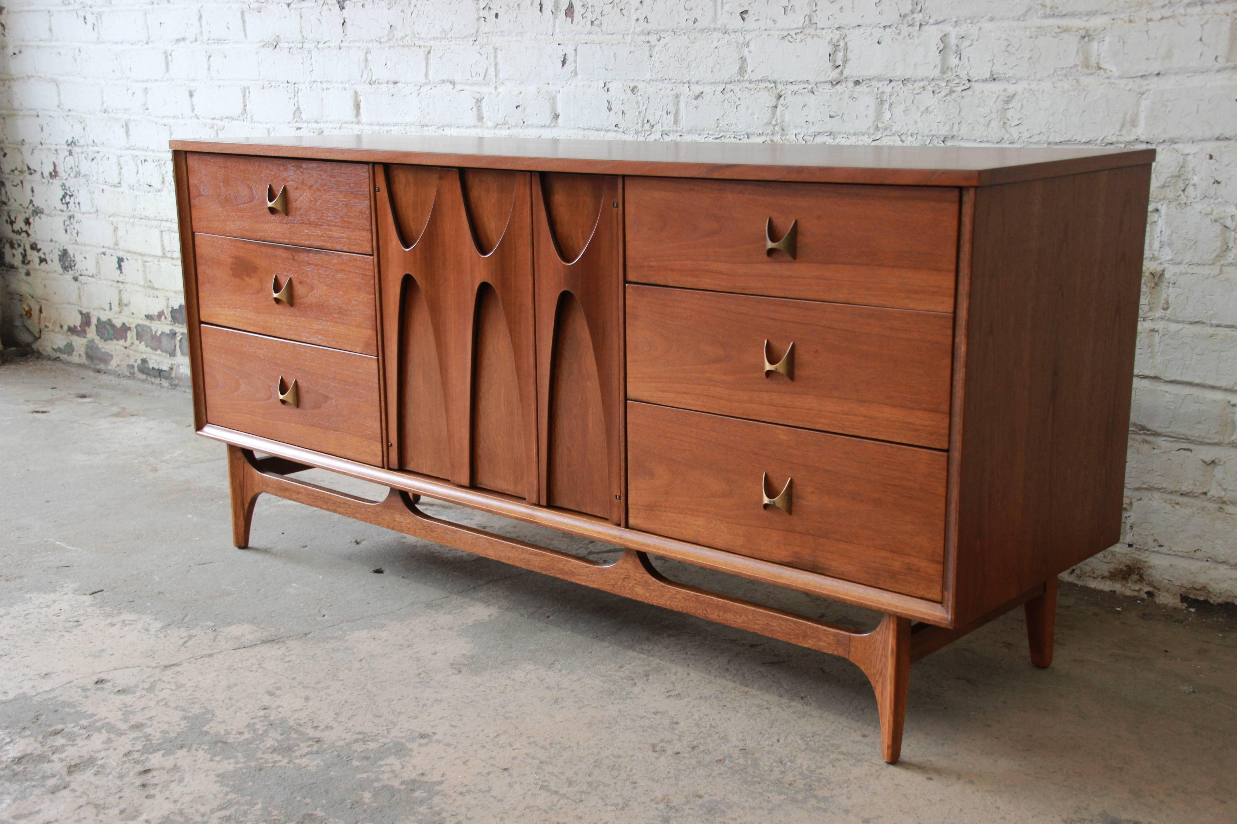 An iconic Broyhill Brasilia Mid-Century Modern sculpted walnut nine-drawer dresser or credenza. The dresser features gorgeous walnut wood grain, with sculpted arches and original pulls. The centre sculpted cabinet doors open up to three drawers,