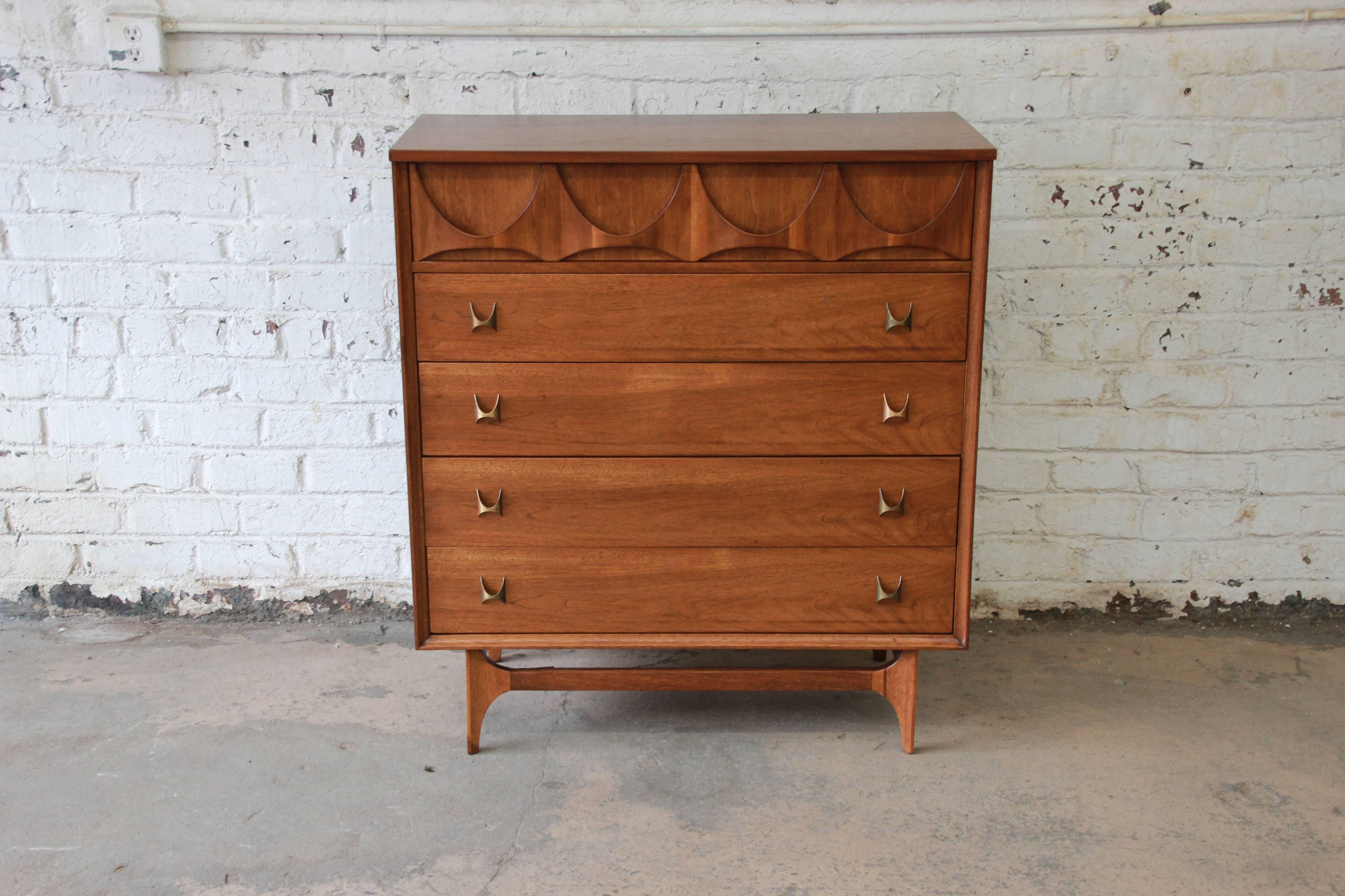 An iconic Broyhill Brasilia Mid-Century Modern sculpted walnut five-drawer highboy dresser. The dresser features gorgeous walnut wood grain, with sculpted arches and original pulls. It offers ample room for storage, with five deep dovetailed