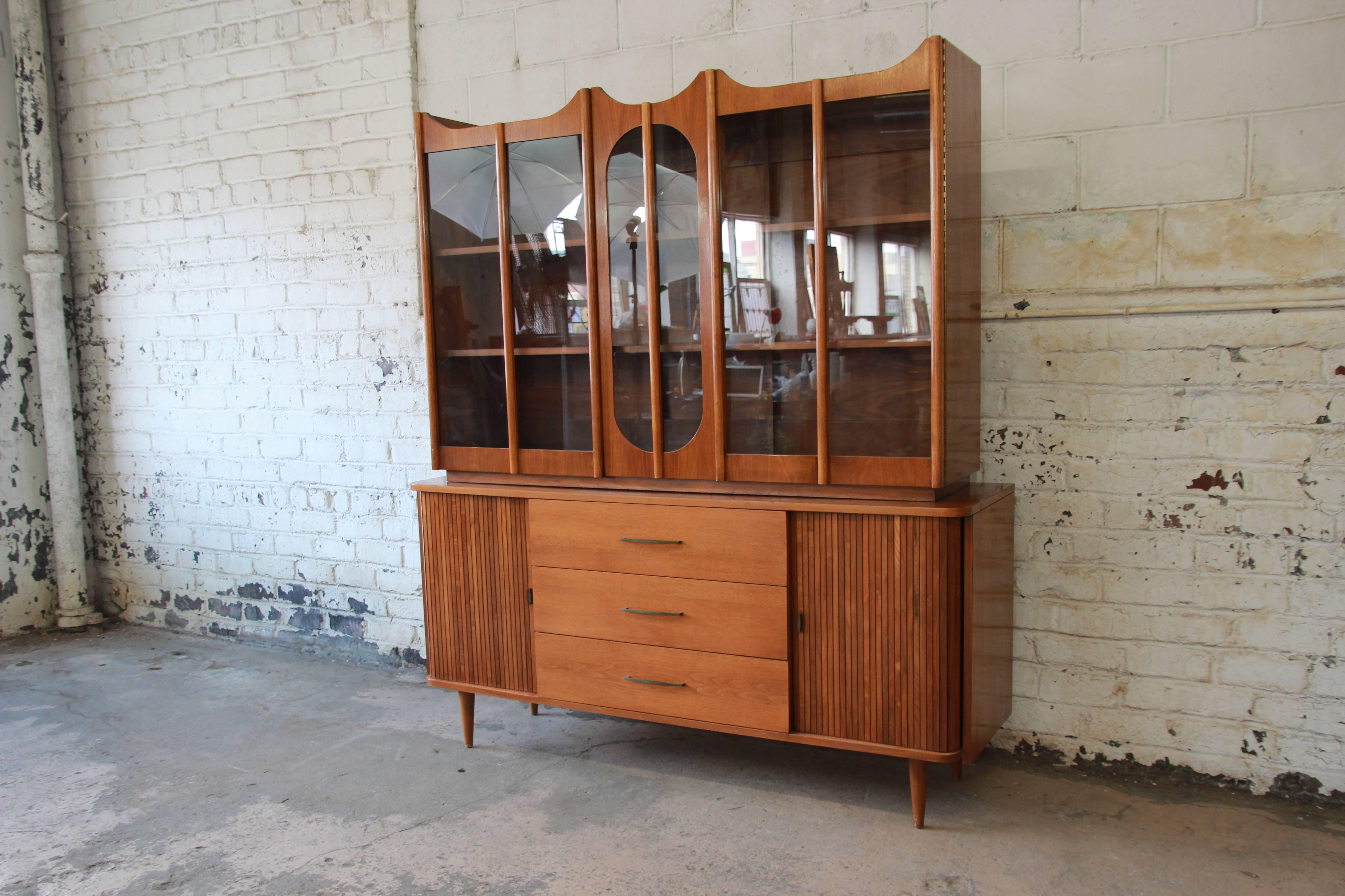 A nice Mid-Century Modern sideboard credenza with glass front hutch top. The sideboard features gorgeous walnut wood grain and sliding tambour doors. It offers ample room for storage, with three lower drawers in the centre and two cabinet spaces and