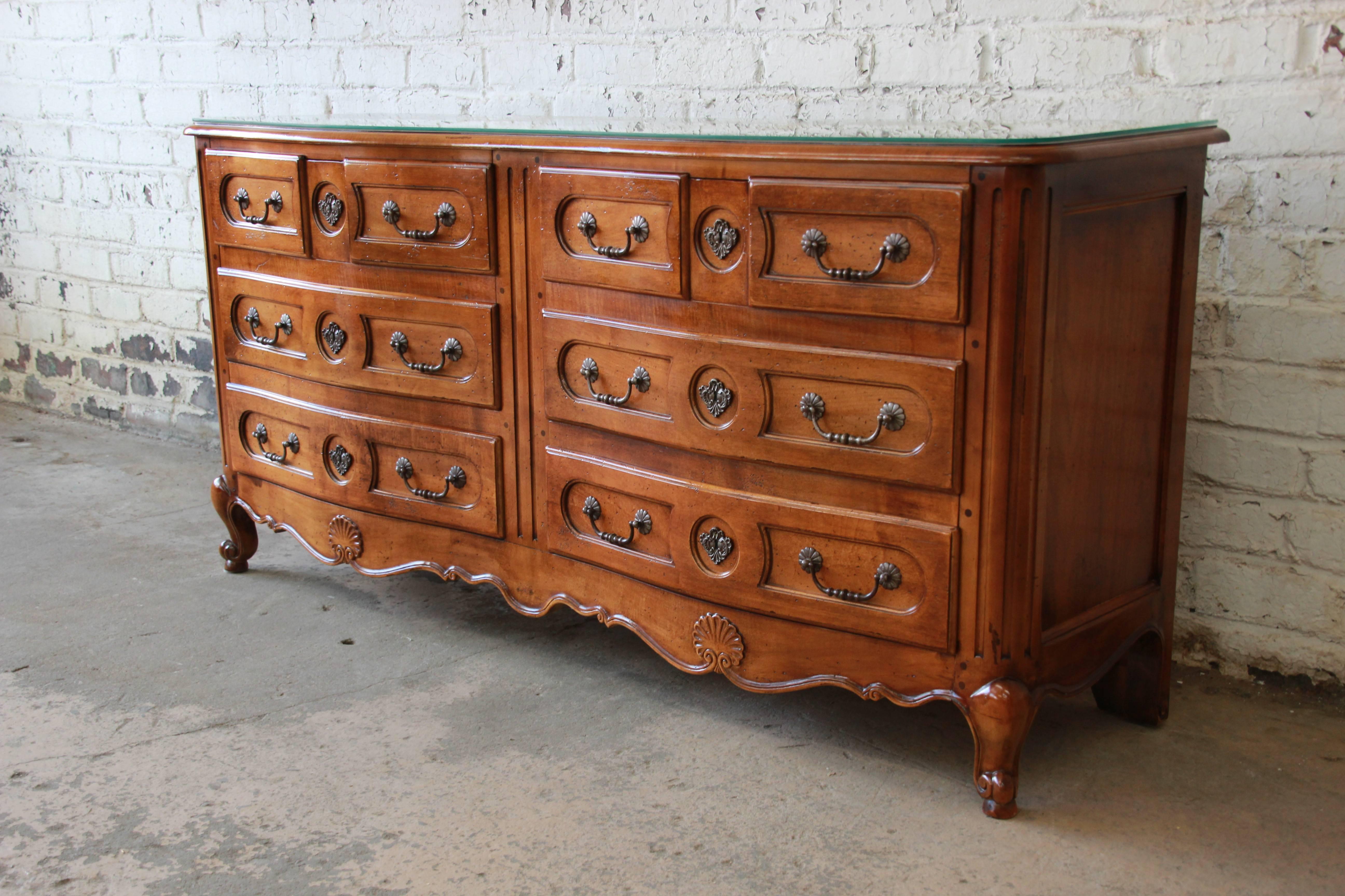 An outstanding solid cherrywood double dresser from the Pierre Deux French Country collection by Henredon. The dresser features stunning carved wood details with a shell motif, original hardware, and a Louis XV style. It offers ample room for