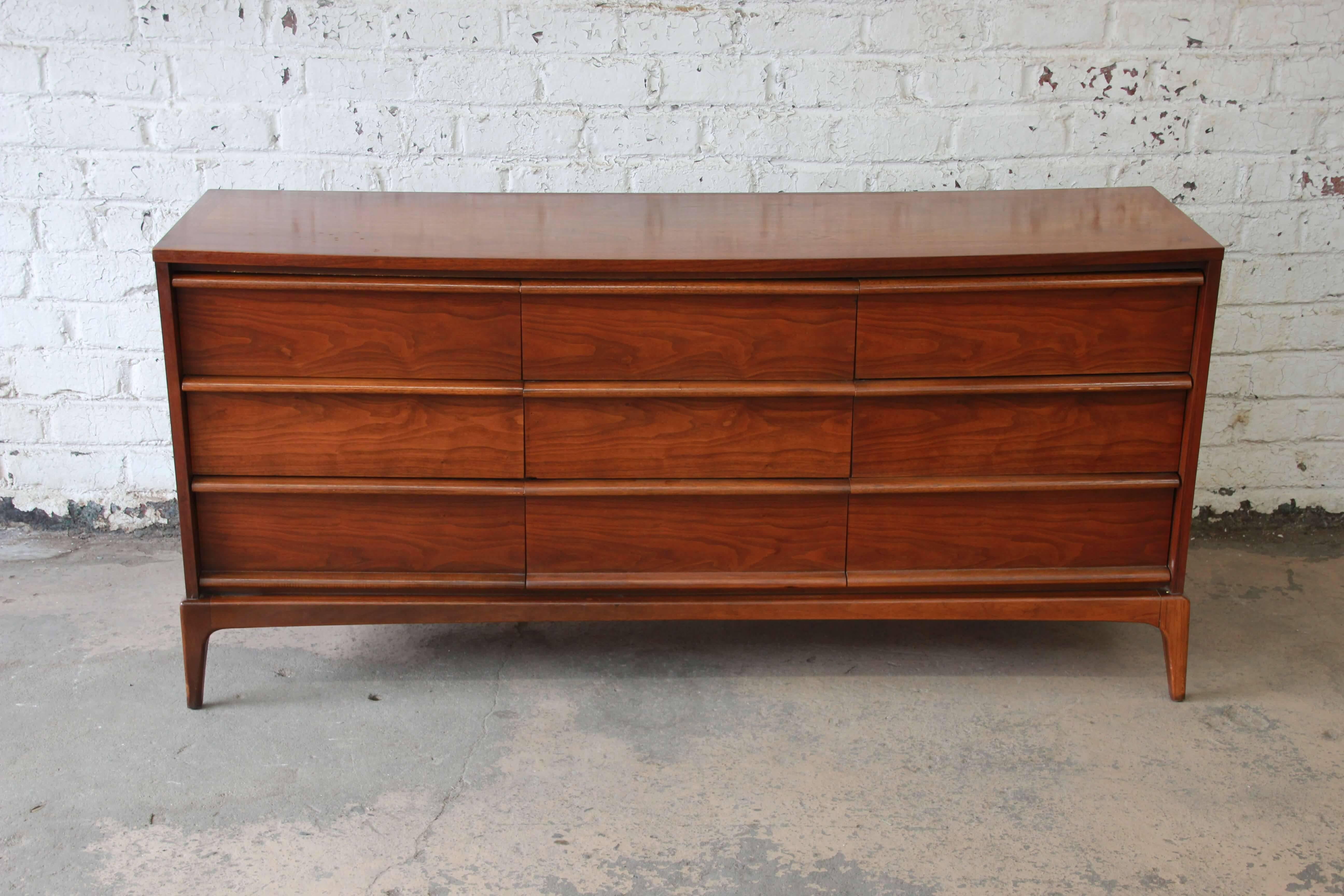 Offering a very nice Mid-Century Modern triple dresser or credenza by Lane. The piece features nine smooth sliding drawers with round sculpted pulls that offers lots of room for storage. It has a nice walnut wood grain with tapered legs. The dresser