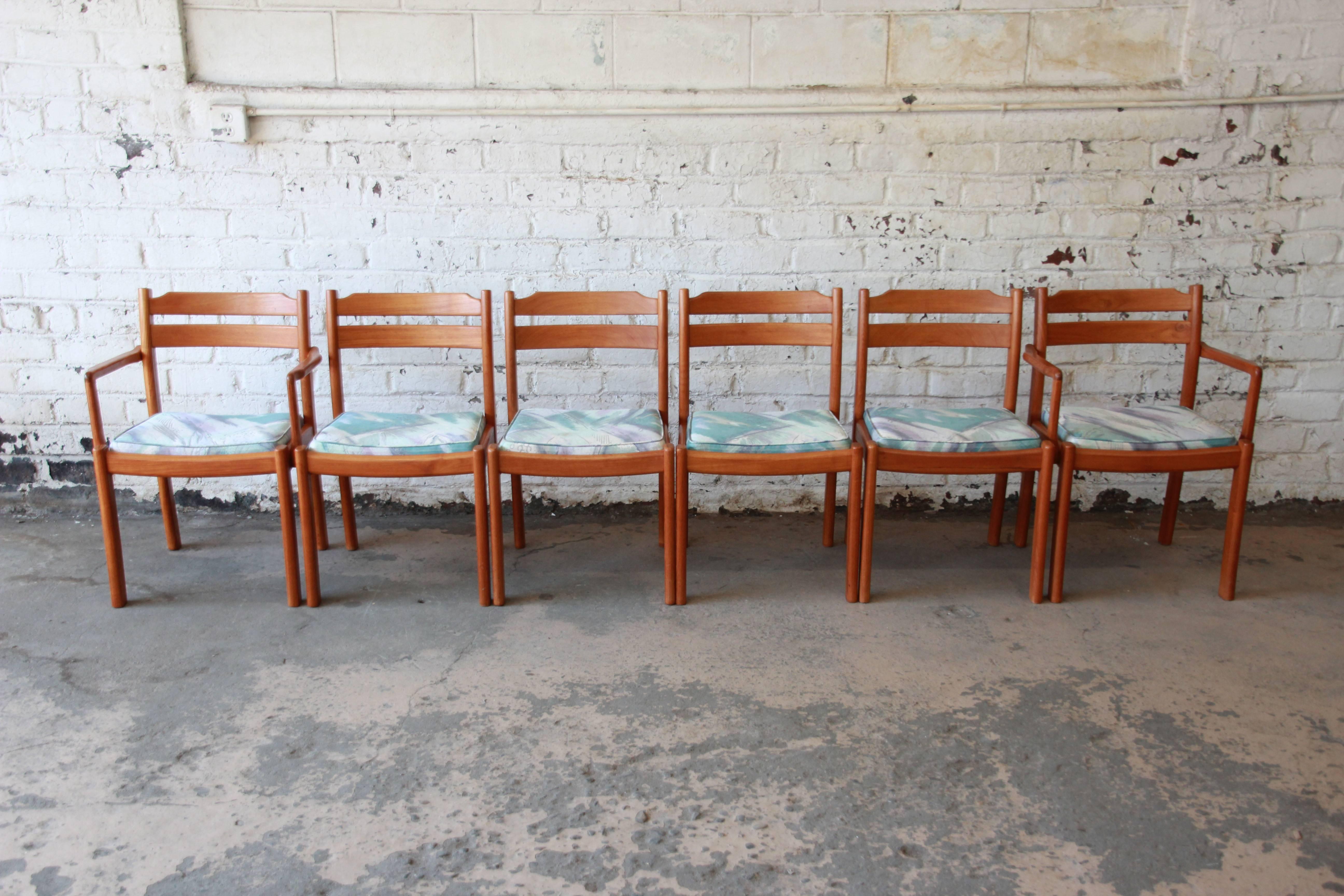 A nice set of six solid teak dining chairs made in Denmark by Dyrlund. The chairs feature solid sculpted teak construction and original vintage upholstery in white, teal, and purple. The set includes two captain chairs and four side chairs. The