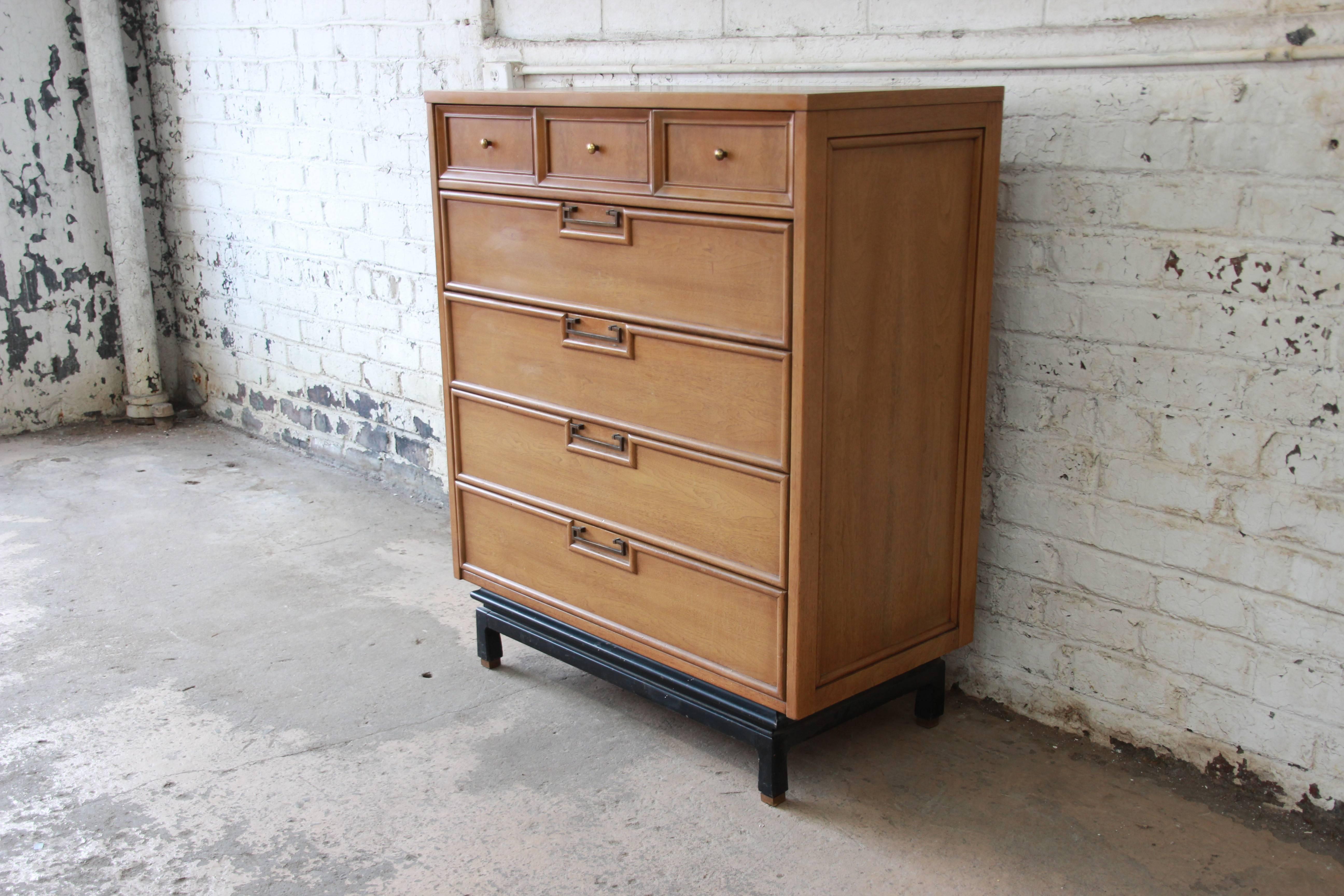 A gorgeous Mid-Century Modern Hollywood Regency chinoiserie highboy dresser by American of Martinsville. The dresser features beautiful bleached walnut wood grain and original brass drawer pulls. It is accented with a sculpted black lacquered base,