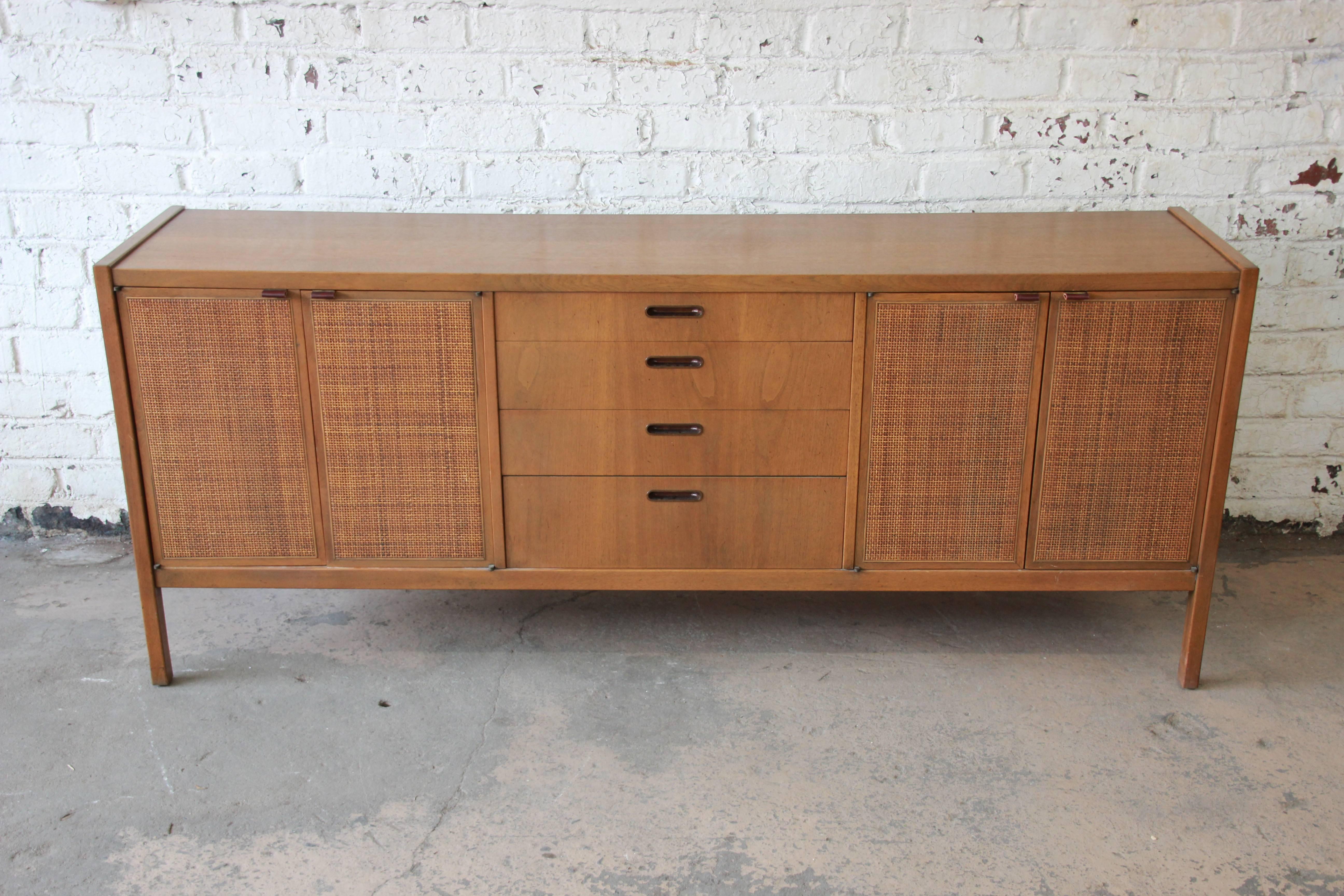 Offering a very nice Mid-Century Modern credenza with woven front doors by Founders. This credenza has two woven front cabinet doors on each side with genuine leather pulls. The doors open up to an adjustable shelf for storage. The center has four