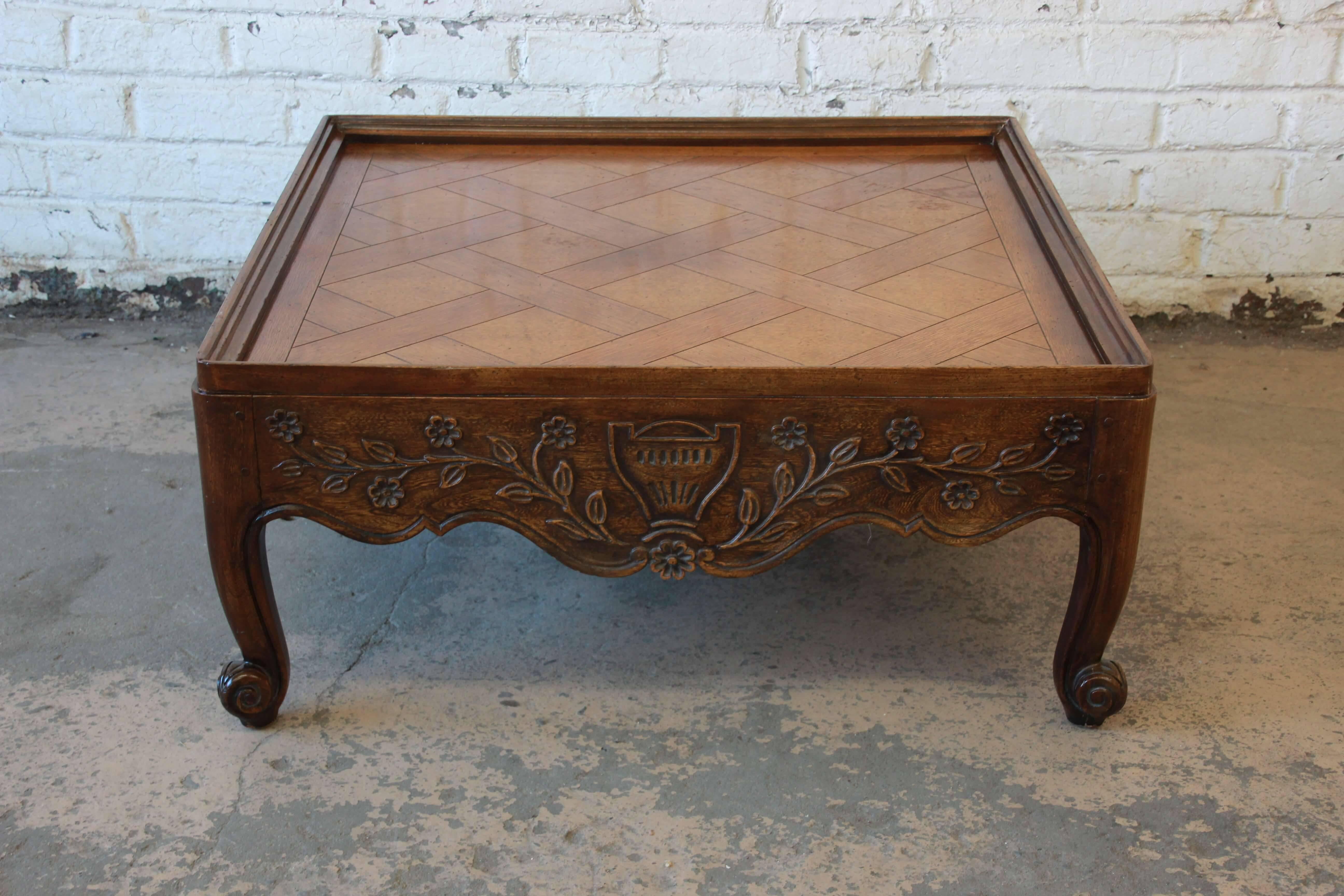 Offering a very nice carved French Country square coffee table by Baker Furniture. The coffee table has beautiful floral carved details with classic Provincial legs. It features a nice parquetry design on top. The table is in good vintage condition