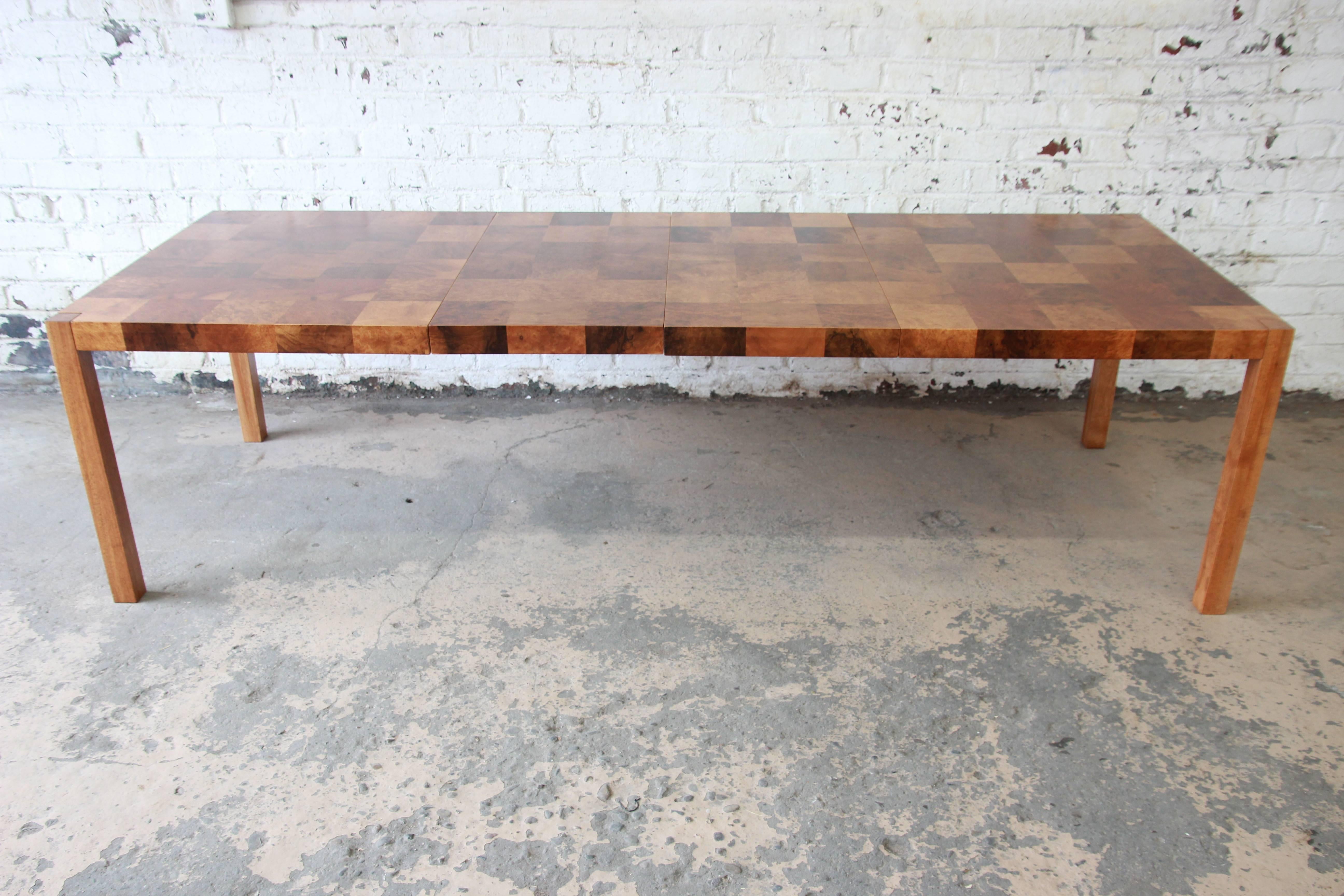 Offering an exceptional Mid-Century Modern patchwork burl wood Parsons extension dining table designed by Milo Baughman. This truly one-of-a-kind table features gorgeous burled olive wood grain and sleek and stylish midcentury design. Extends to