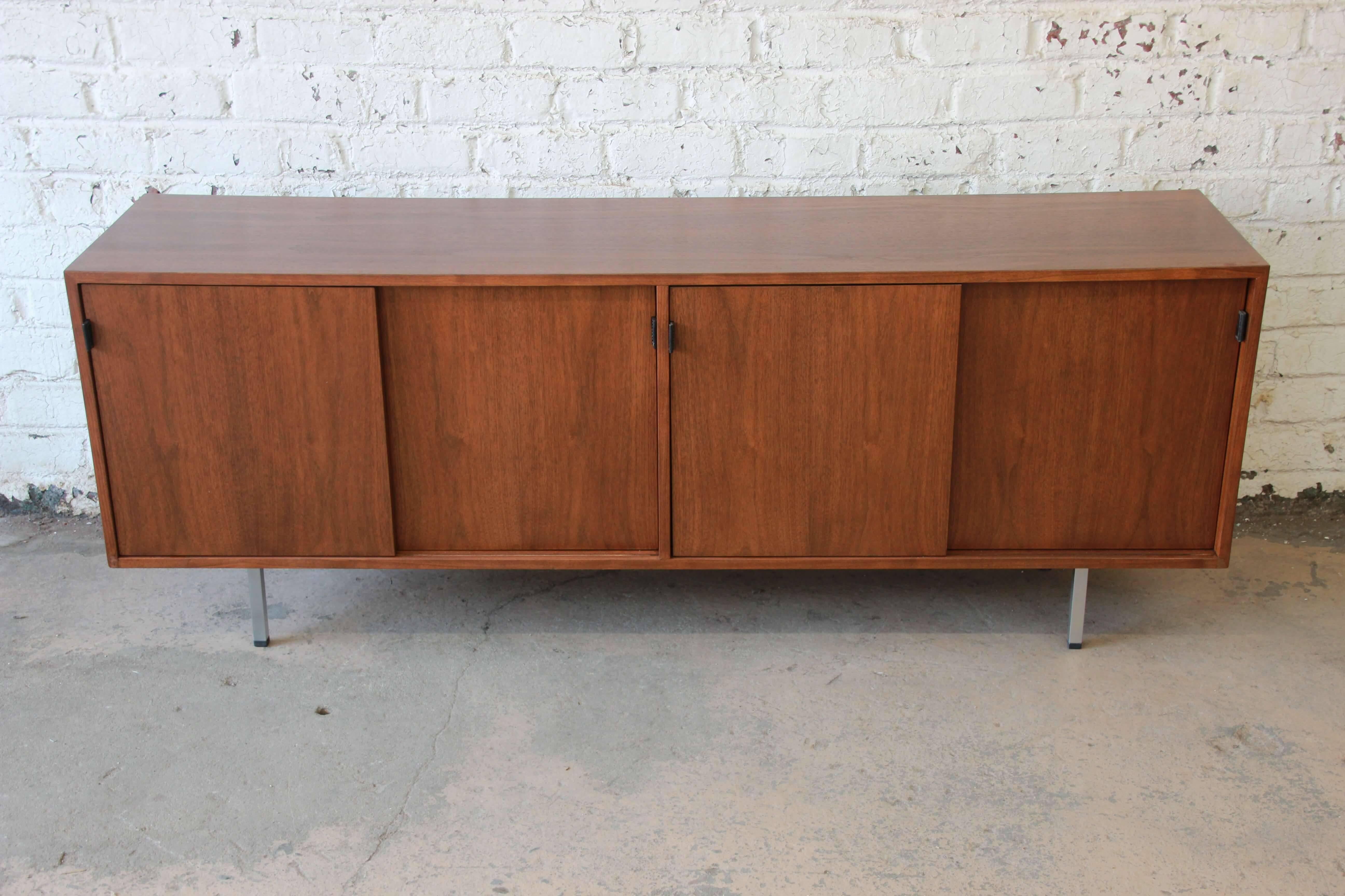 Offering a stunning newly restored Mid-Century Modern walnut credenza by Florence Knoll. This credenza has polished chrome legs supporting the beautiful walnut credenza case. There are four sliding doors with genuine leather pulls. The left door